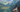 A dark-haired woman looks out over a scenic alpine lake.