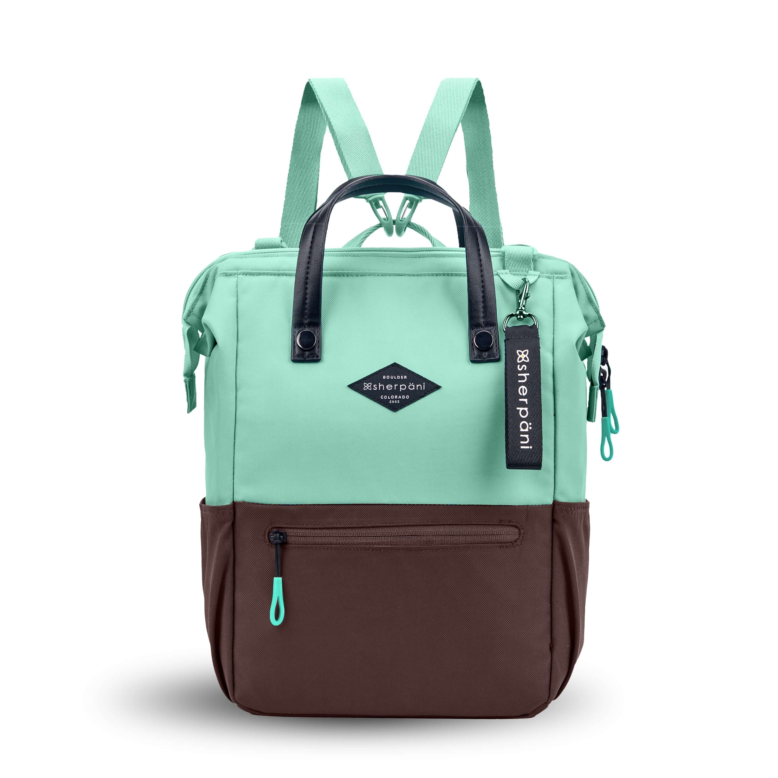 Flat front view of Sherpani three-in-one bag, the Dispatch in Seagreen. The bag is two-toned: the top is light green and the bottom is brown. There is an external zipper pocket on the front panel. Easy-pull zippers are accented in light green. A branded Sherpani keychain is clipped to the upper right corner. Elastic water bottle holders sit on either side of the bag. It has short tote handles and adjustable/detachable straps that can function for a backpack or crossbody. 