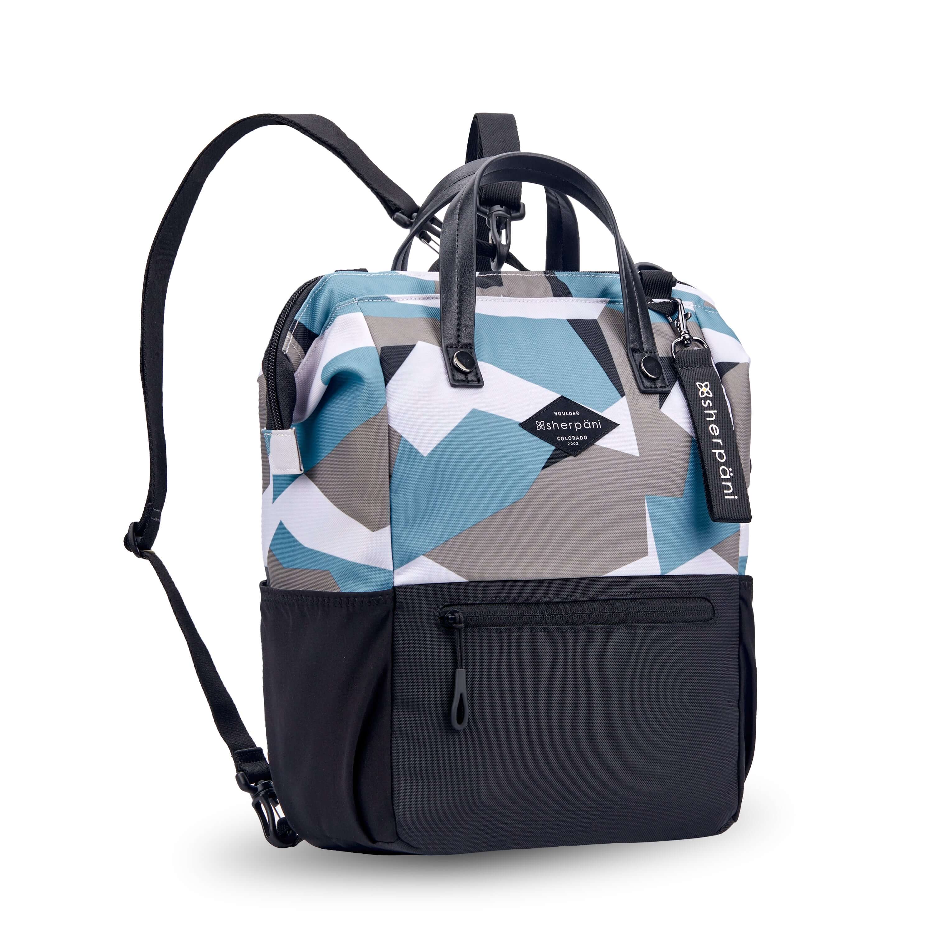 Angled front view of Sherpani three in one bag, the Dispatch in Summer Camo. The bag is two toned: the top is a camouflage pattern of light blue, gray and white, the bottom is black. There is an external zipper pocket on the front panel. Easy pull zippers are accented in black. A branded Sherpani keychain is clipped to the upper right corner. Water bottle holders sit on either side of the bag. It has short tote handles and adjustable straps that can function for a backpack or crossbody. 