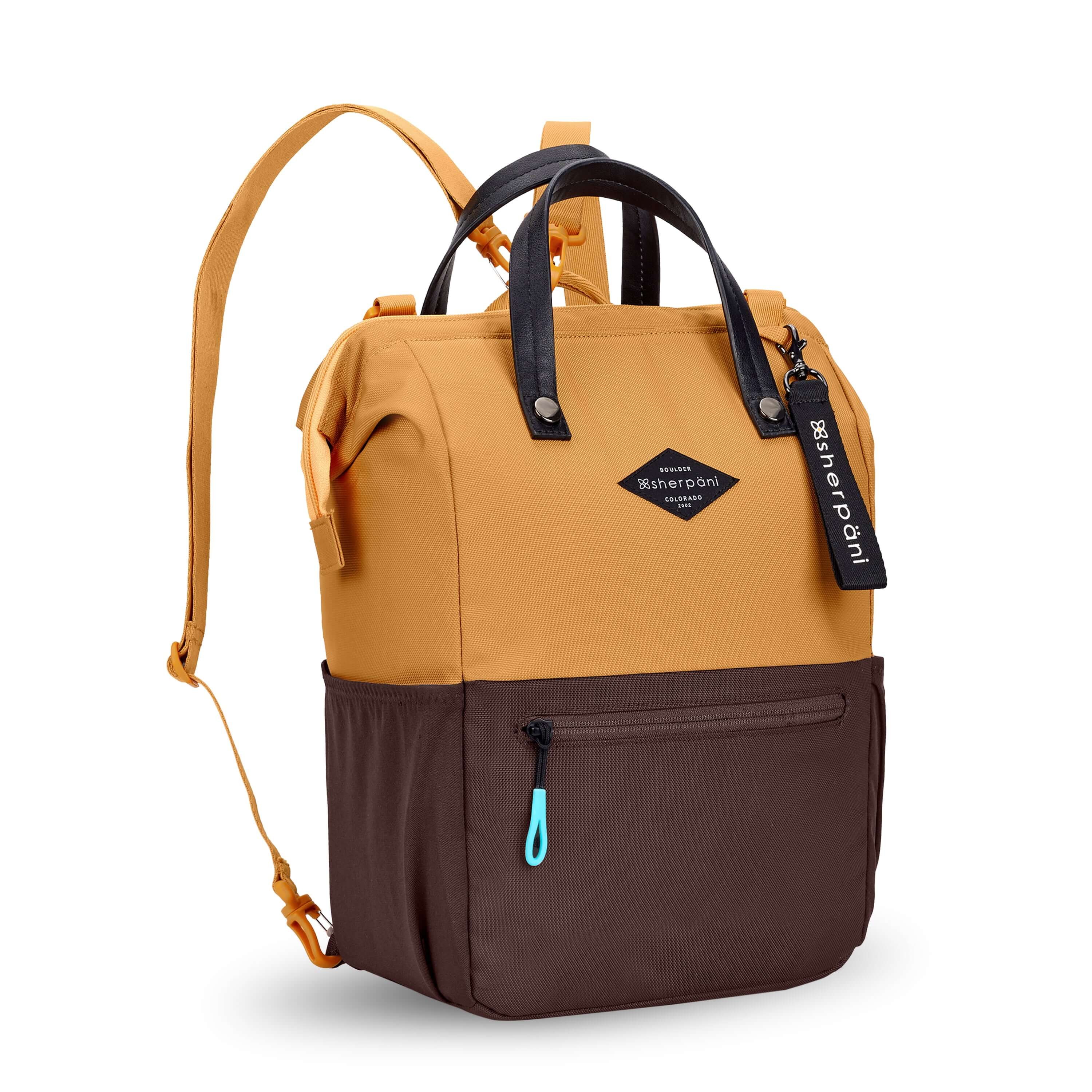 Angled front view of Sherpani three in one bag, the Dispatch in Sundial. The bag is two toned: the top is burnt yellow and the bottom is brown. There is an external zipper pocket on the front panel. Easy pull zippers are accented in aqua. A branded Sherpani keychain is clipped to the upper right corner. Elastic water bottle holders sit on either side of the bag. It has short tote handles and adjustable/detachable straps that can function for a backpack or crossbody. 