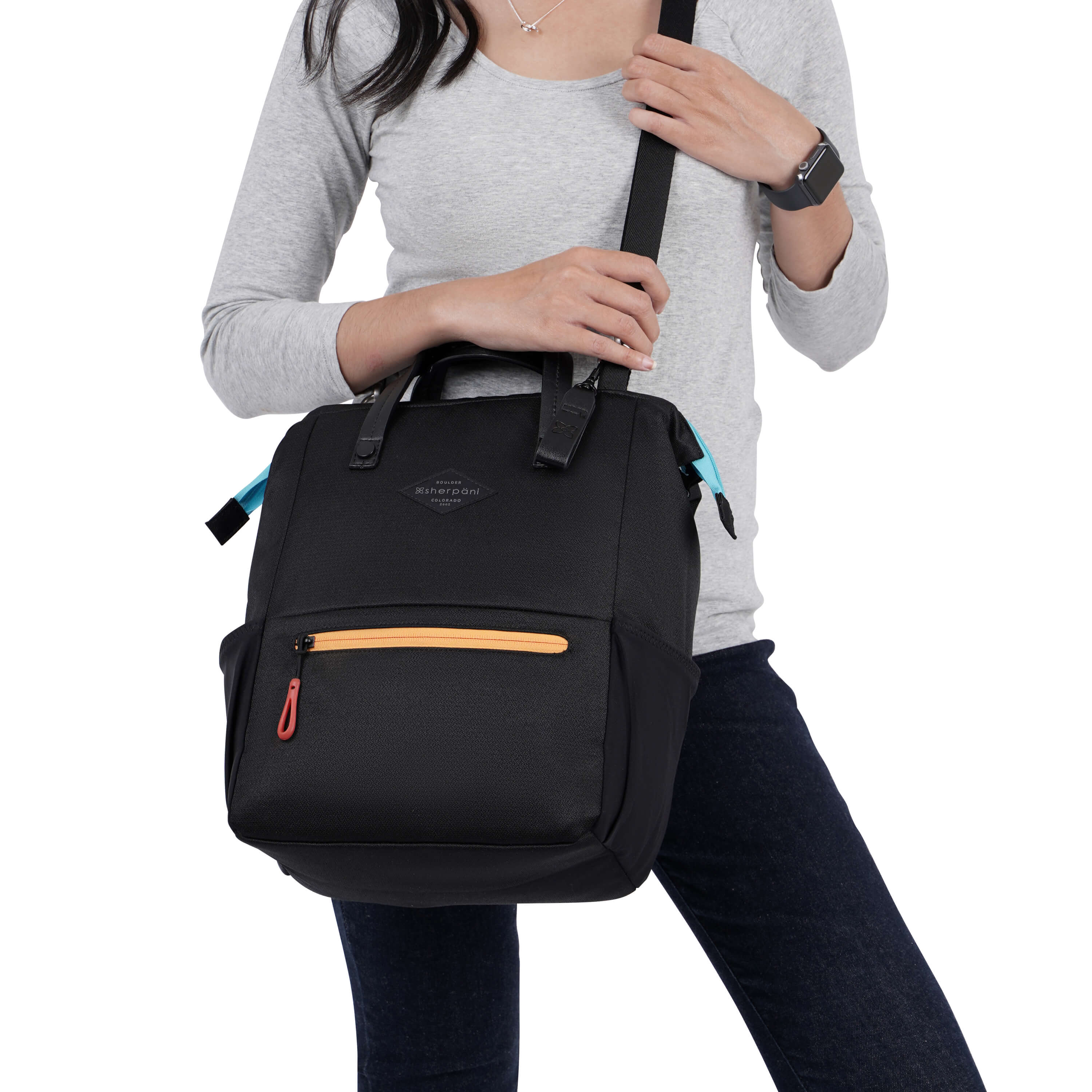 Close up view of a dark haired model facing the camera. She is wearing a gray top and black pants. She carries Sherpani three-in-one bag, the Dispatch in Chromatic, as a cossbody. 