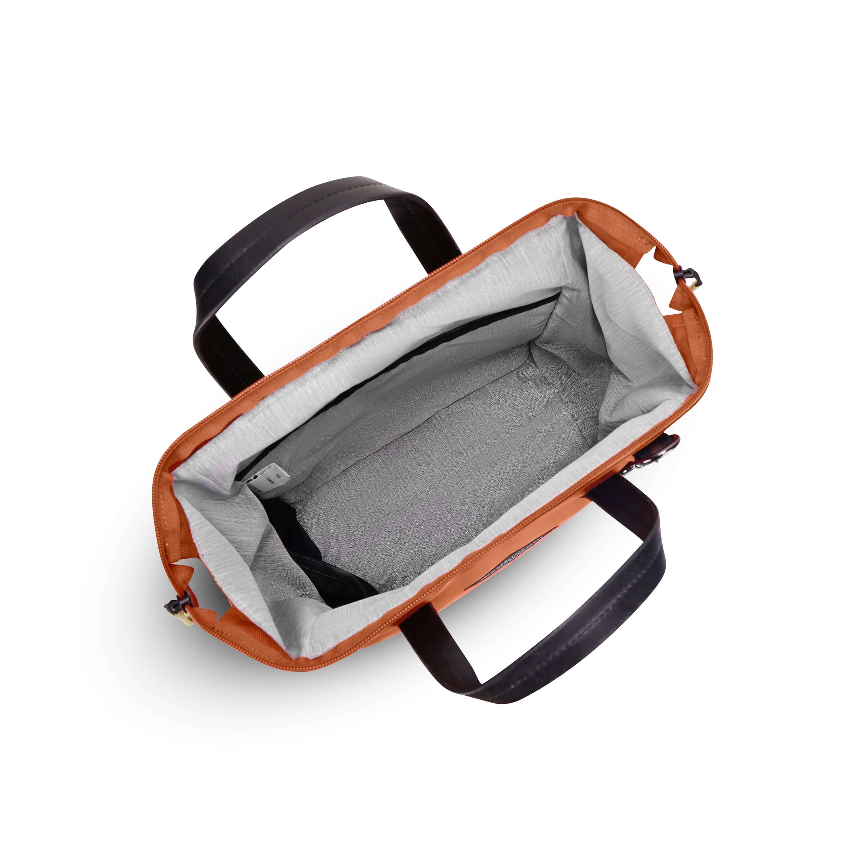 Top view of Sherpani three-in-one bag, the Dispatch in Clay. The main zipper compartment is open to reveal a doctor bag style opening with a rectangular metal frame. The inside of the bag is light gray and features an internal pouch and water bottle holder. 
