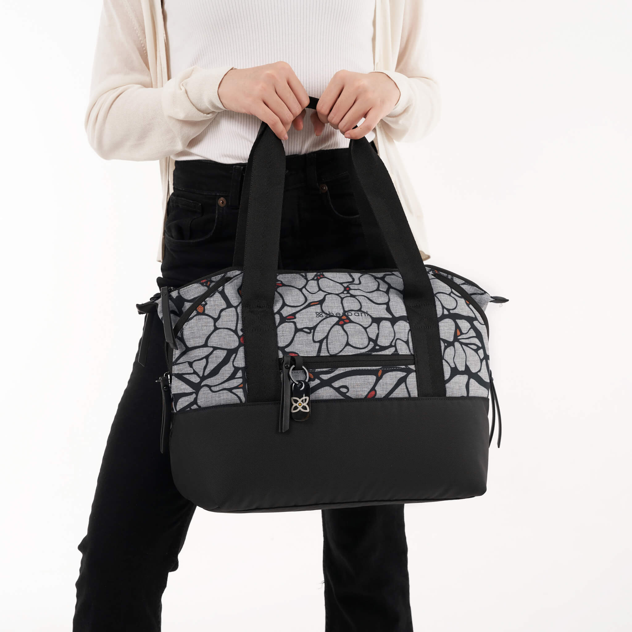 A model holding Sherpani travel tote, the Eclipse in Sakura, by the tote bag handles. 