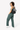 Model smiling over her left shoulder with one hand in her pocket, wearing the Sherpani sling bag, the Esprit in Magnolia on her back. #color_magnolia