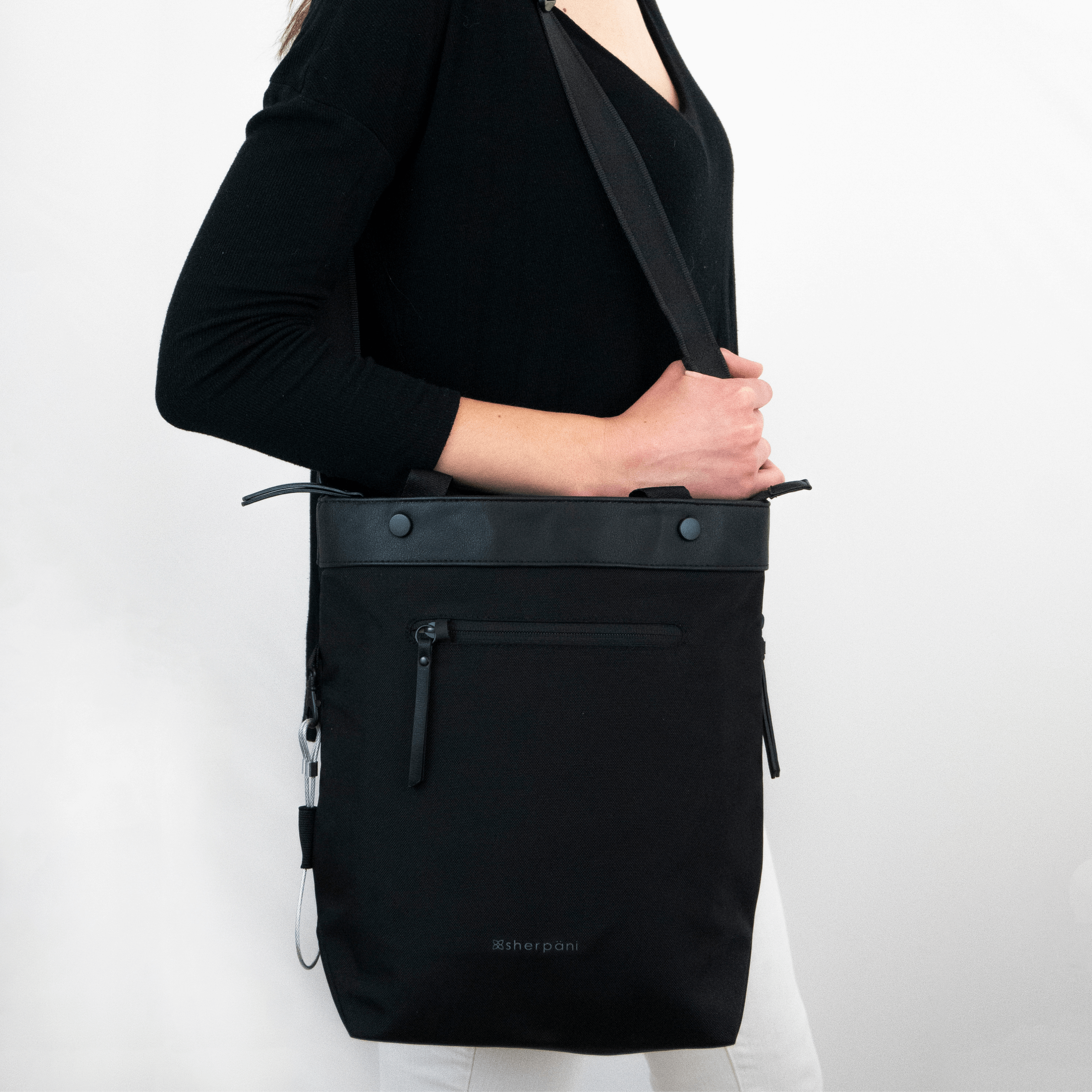 Close up view of a model facing the side. She is wearing a black shirt, white pants, and Sherpani's Anti-Theft bag, the Geo AT in Carbon, over her shoulder. 
