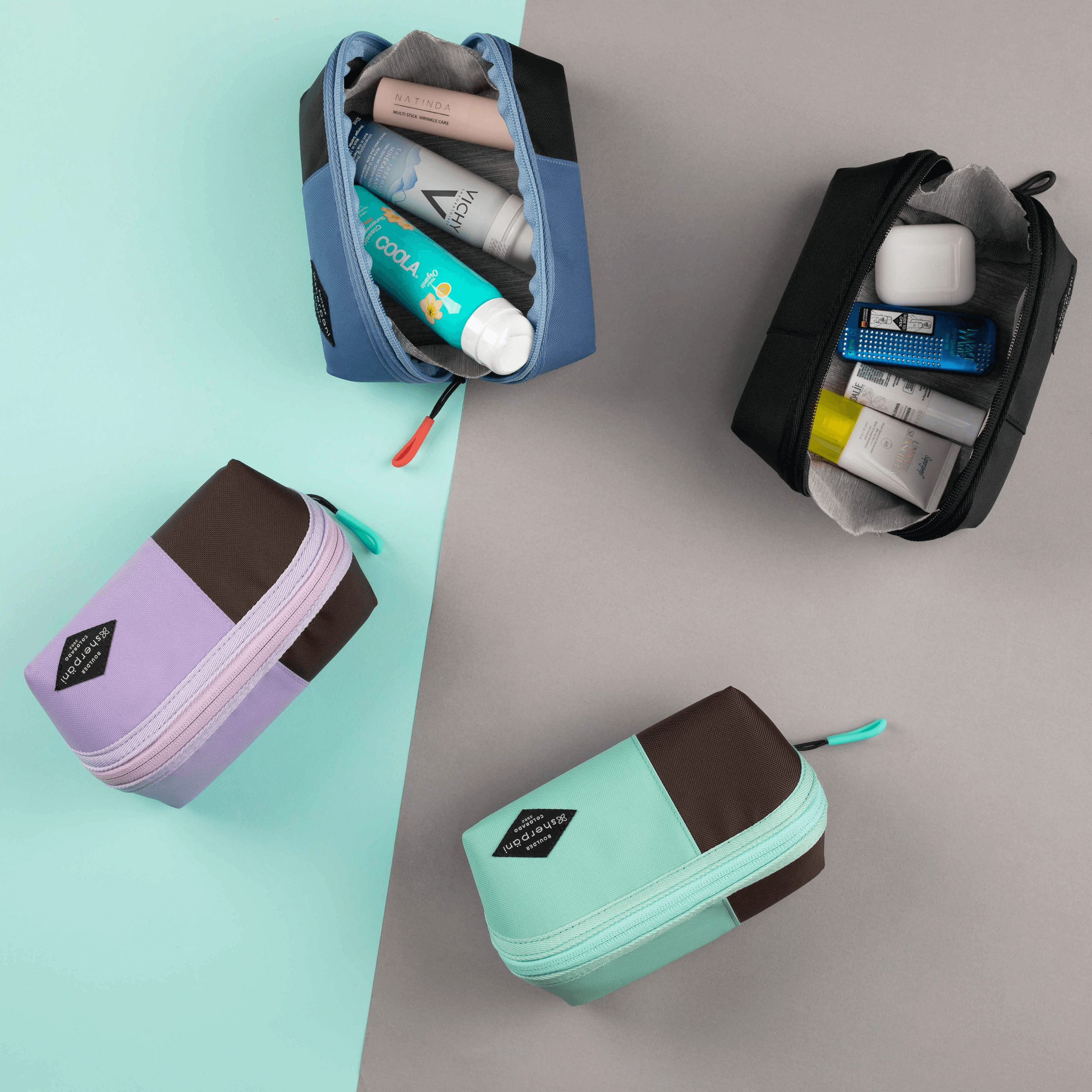 Top view of four Sherpani Harmony travel accessories on a gray and green background. One is Pacific Blue, one is Raven, one is Lavender and one is Seagreen. Two of the pouches are open and full of example items, two of the pouches are closed. #color_seagreen