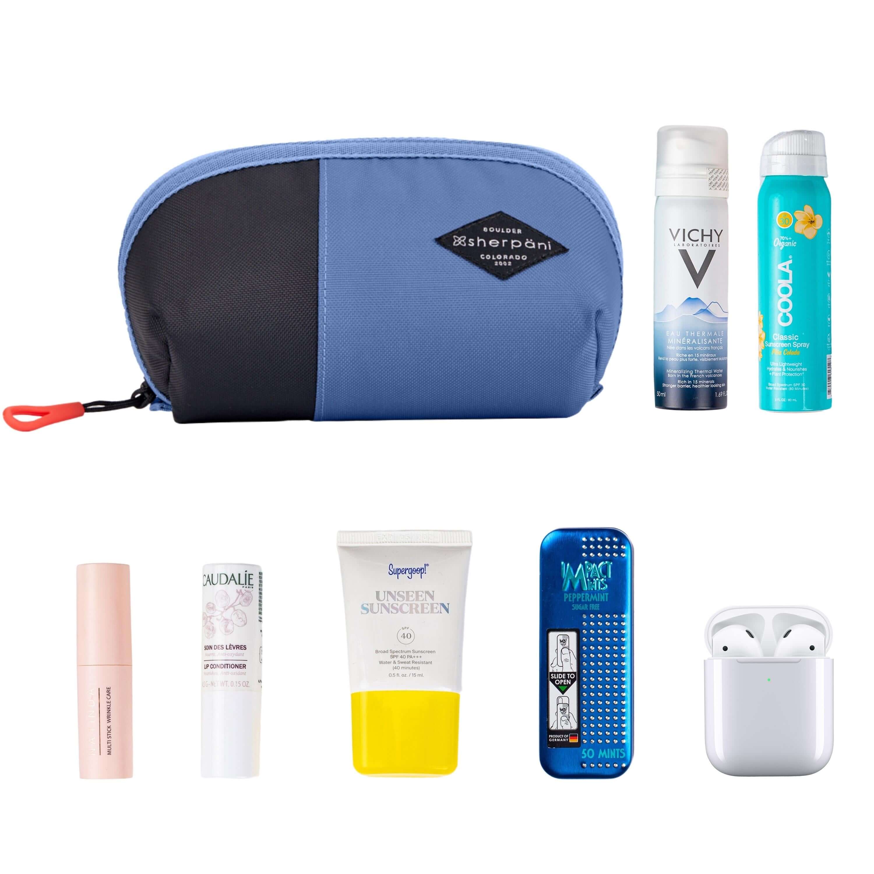 Top view of example items to fill the bag. Sherpani travel accessory, the Harmony in Pacific Blue, is shown in the upper left corner. It is surrounded by an assortment of items: beauty products, skincare products, sunscreen, mints and AirPods. 