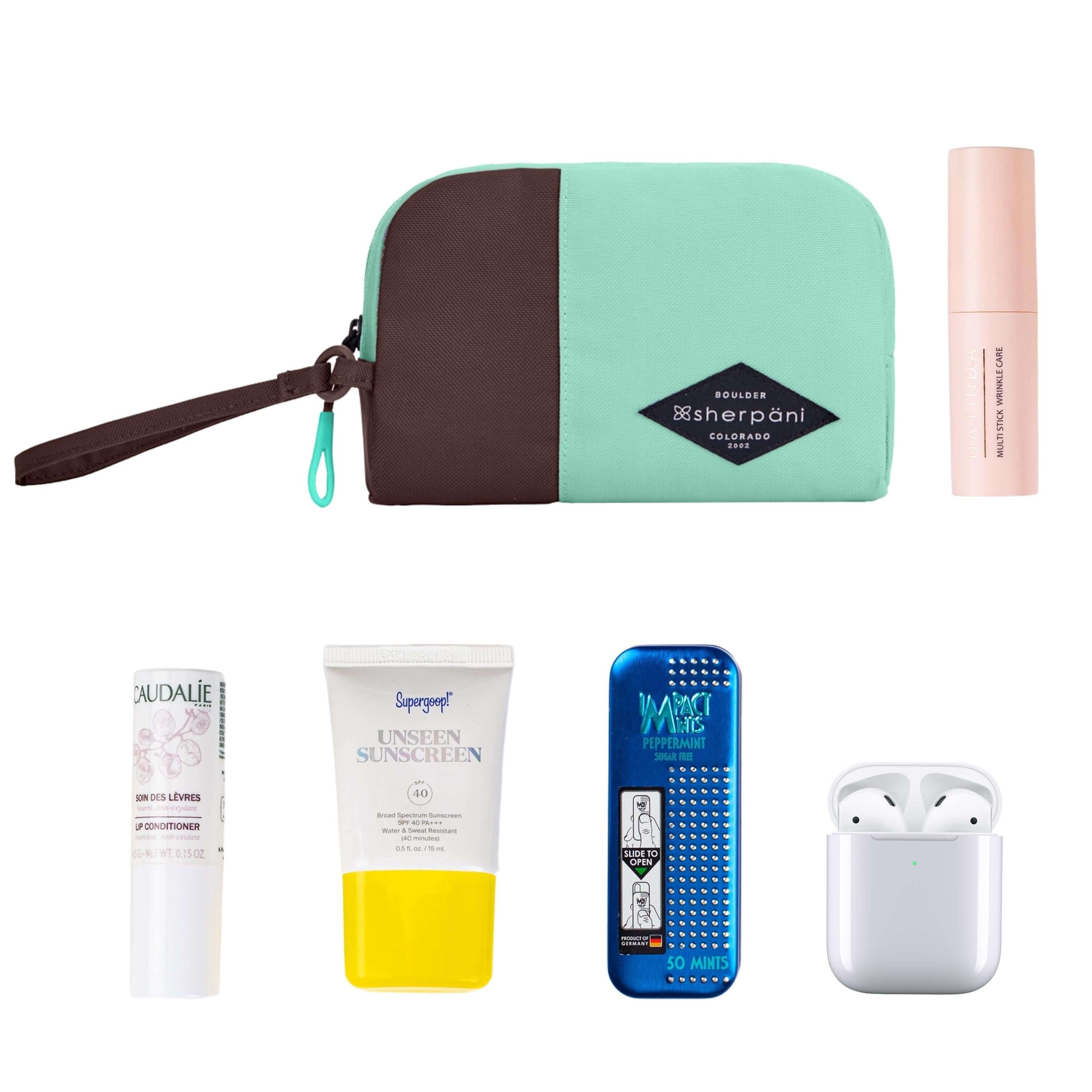Top view of example items to fill the bag. Sherpani travel accessory, the Jolie in Seagreen in small size, lies in the upper left corner. It is surrounded by an assortment of items: beauty product, skincare product, sunscreen, mints and AirPods. 