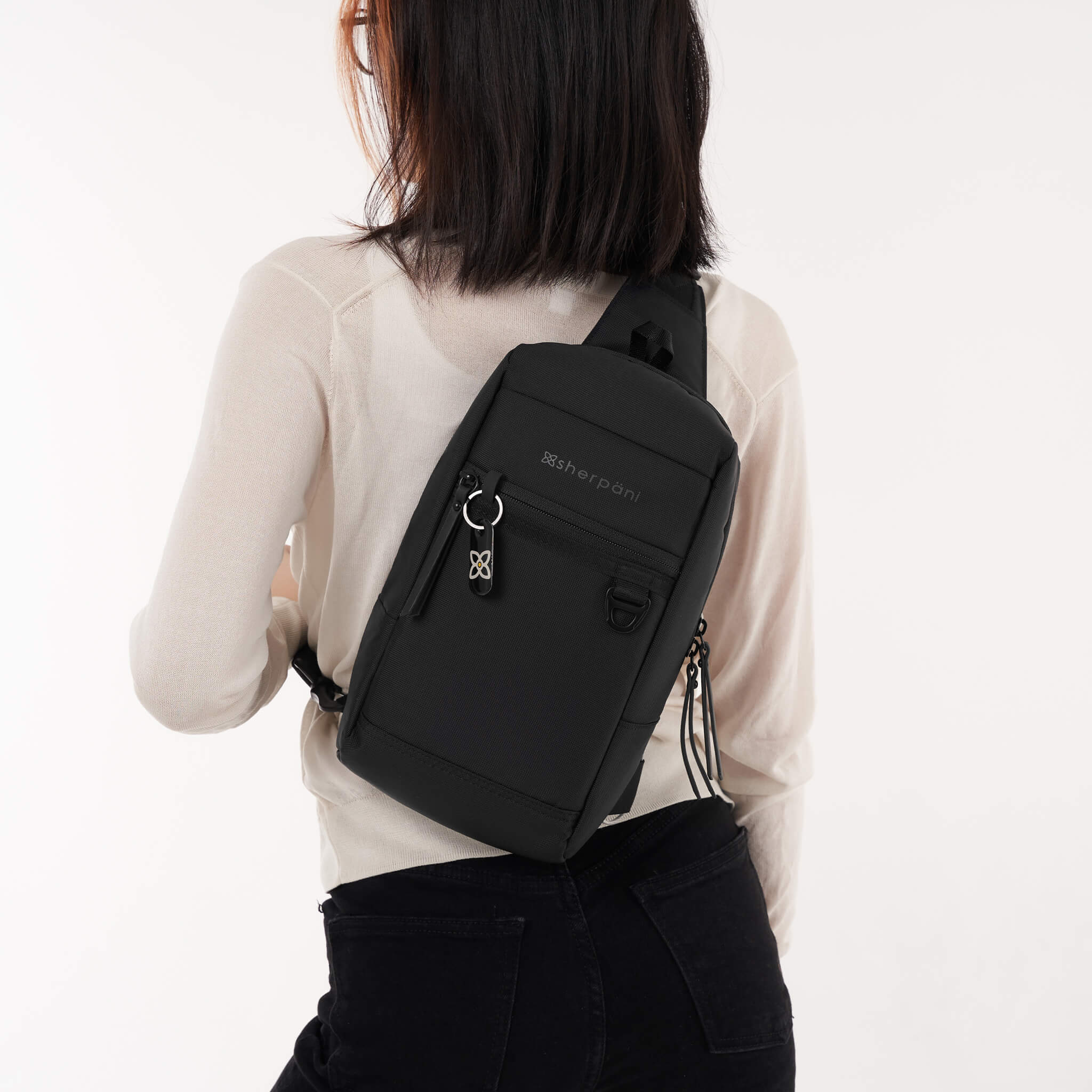 A model wearing Sherpani Anti-Theft sling backpack, the Metro in Carbon. 