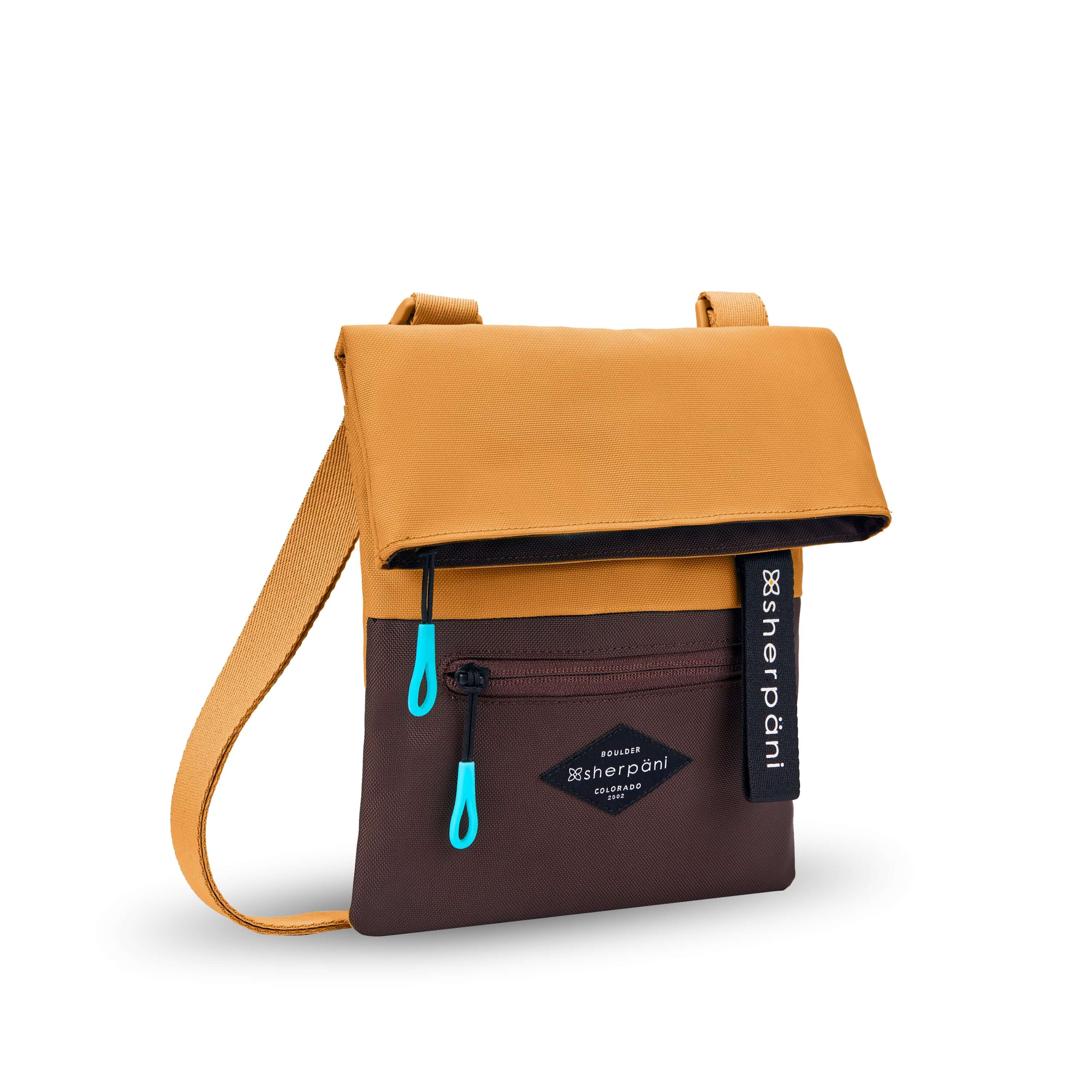 Angled front view of Sherpani crossbody, the Pica in Sundial. The bag is two toned: the top half is burnt yellow and the bottom half is brown. There is an external zipper pocket on the front panel. Easy pull zippers are accented in aqua. The top of the bag folds over creating a signature look. A branded Sherpani keychain is clipped to the upper right corner. The bag has an adjustable crossbody strap. #color_sundial v1