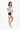Model wearing the Sherpani sling bag, the Prima AT in Straw, on her right shoulder, holding the strap with one hand and gripping the jacket hem with the other, wearing slim-framed glasses. #color_straw-metal
