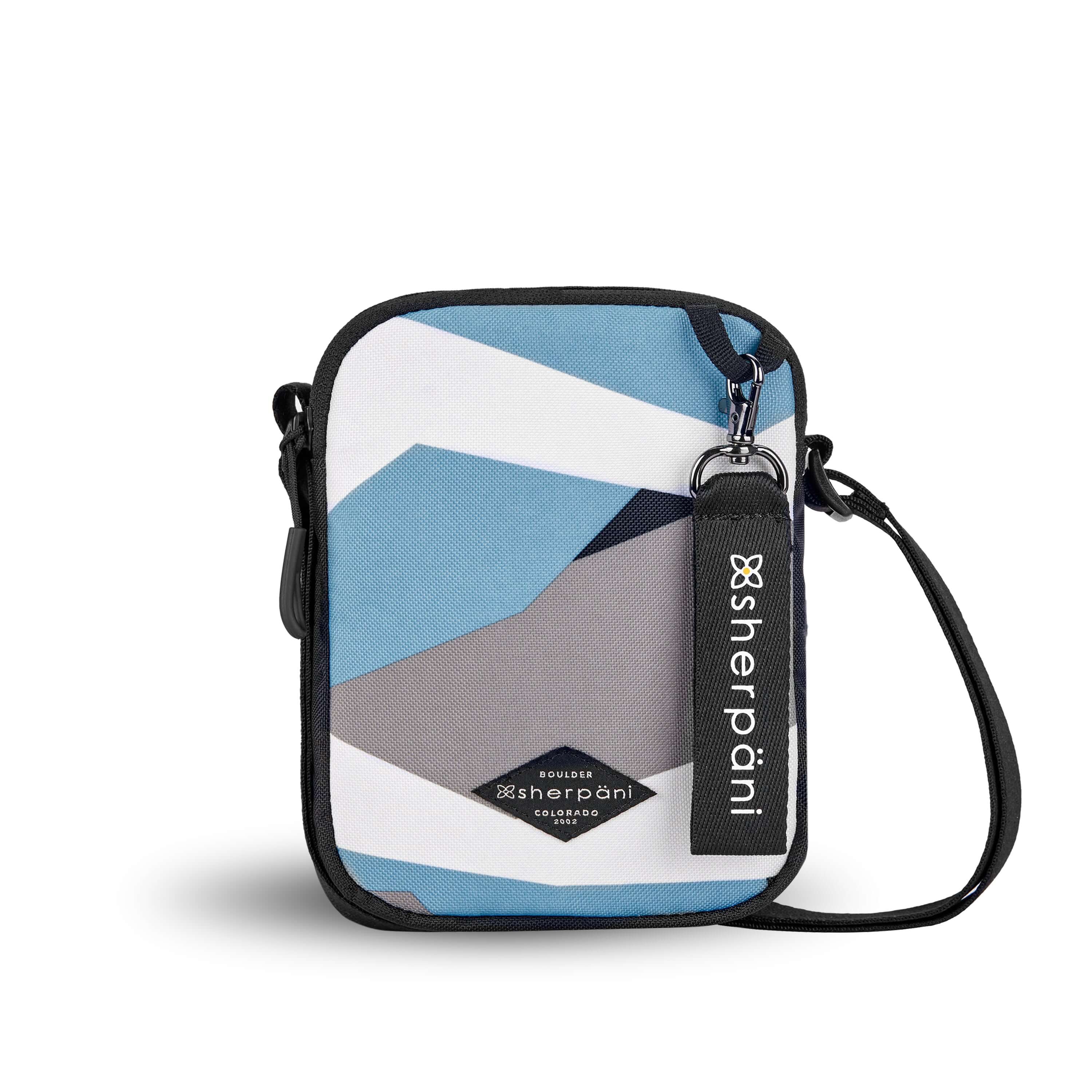 Flat front view of Sherpani crossbody, the Rogue in Summer Camo. The bag is two toned: the front is a camouflage pattern of light blue, gray and white, the back is black. The main zipper compartment features an easy pull zipper accented in black. The bag has an adjustable crossbody strap. A branded Sherpani keychain is clipped to a fabric loop on the top right corner. 