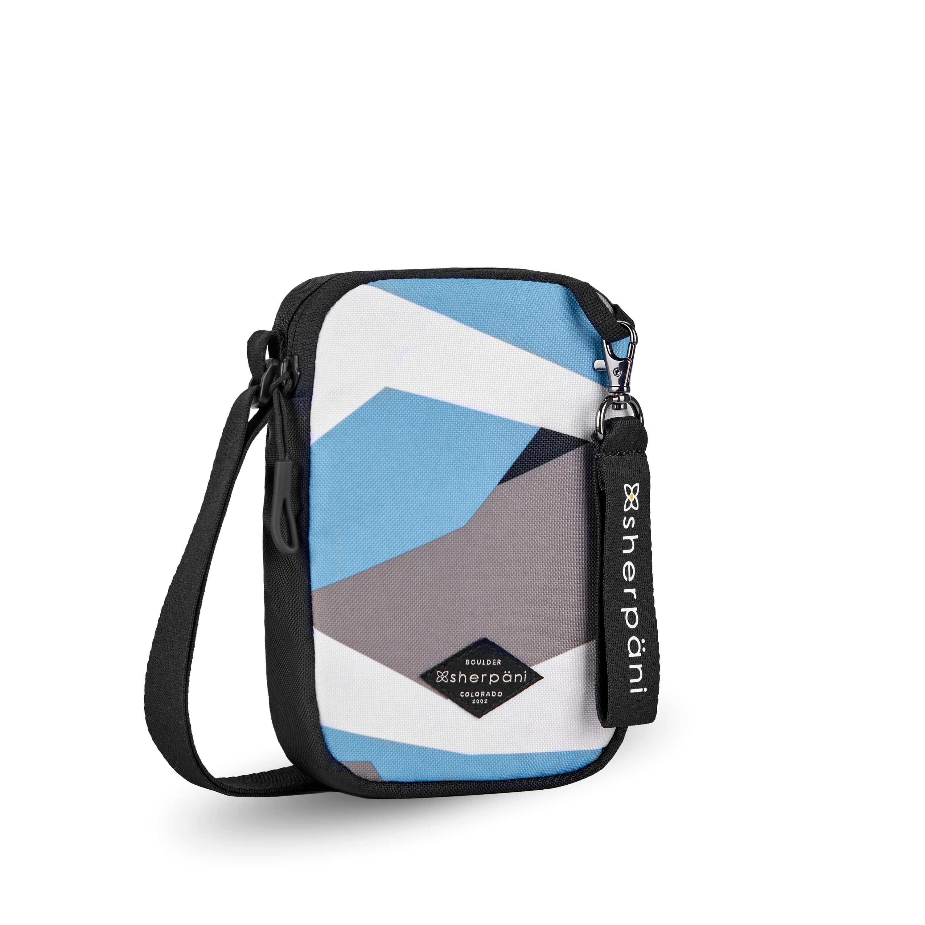 Angled front view of Sherpani crossbody, the Rogue in Summer Camo. The bag is two toned: the front is a camouflage pattern of light blue, gray and white, the back is black. The main zipper compartment features an easy pull zipper accented in black. The bag has an adjustable crossbody strap. A branded Sherpani keychain is clipped to a fabric loop on the top right corner. #color_summer camo
