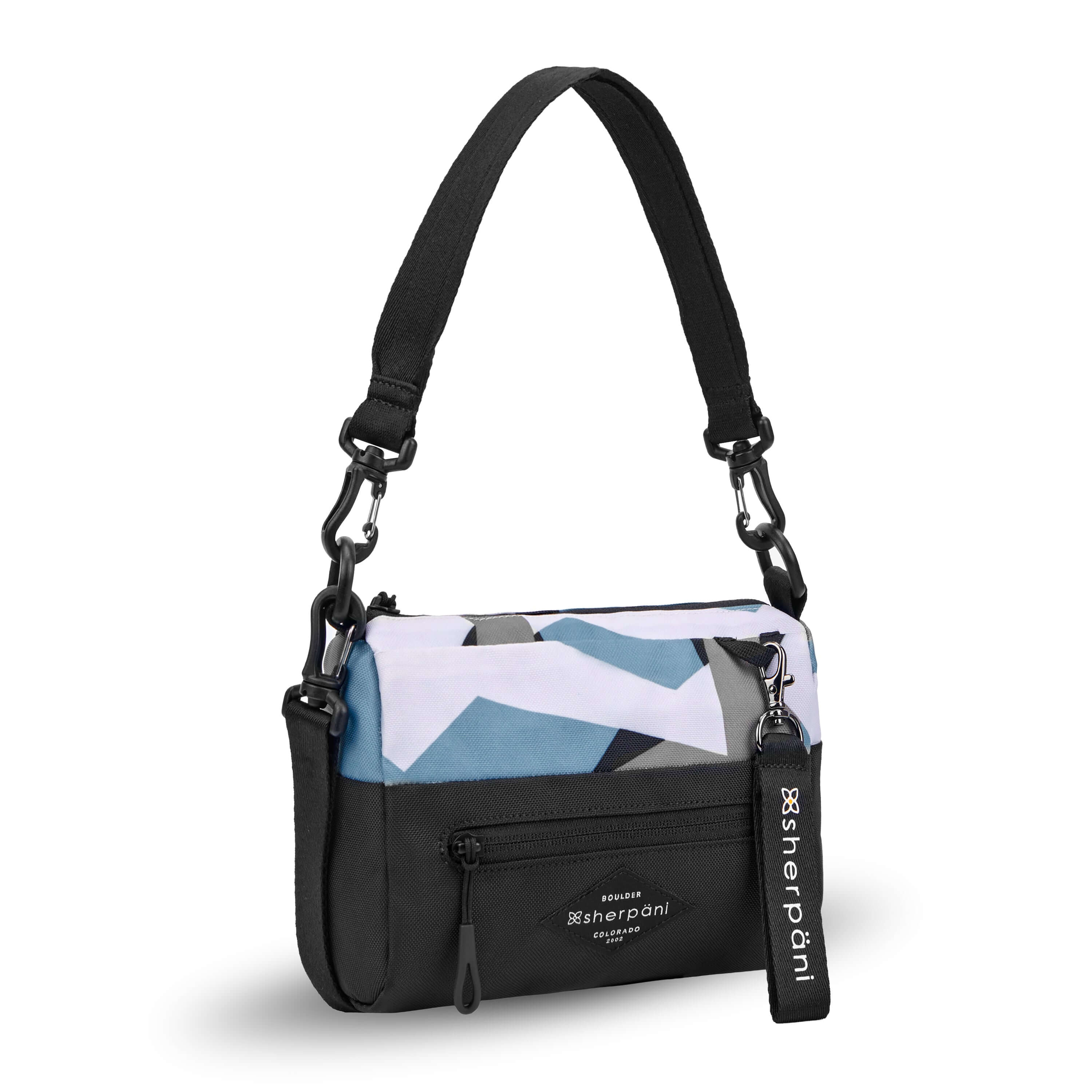 Angled front view of Sherpani's purse, the Skye in Summer Camo. It is two toned, the top half of the bag is a camouflage pattern of white, gray and blue and the bottom half of the bag is black. There is an external zipper compartment with an easy pull zipper accented in black. There is a branded Sherpani keychain clipped to the upper right corner. The bag has a detachable short strap and a longer detachable/adjustable crossbody strap. #color_summer camo
