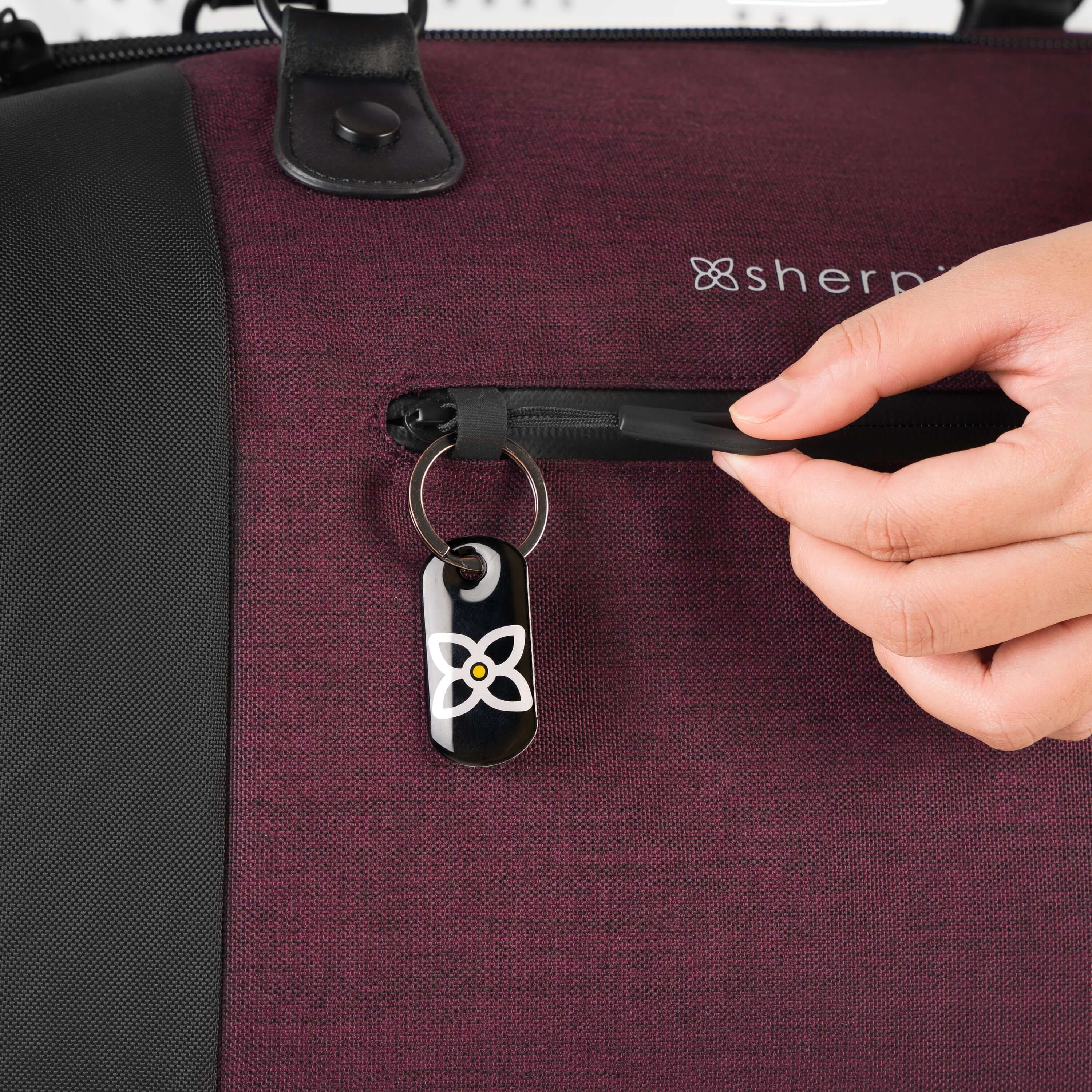 Close up view of a model's hands demonstrating the zipper lock feature on Sherpani's Anti-Theft rolling duffle the Tip in Merlot. 