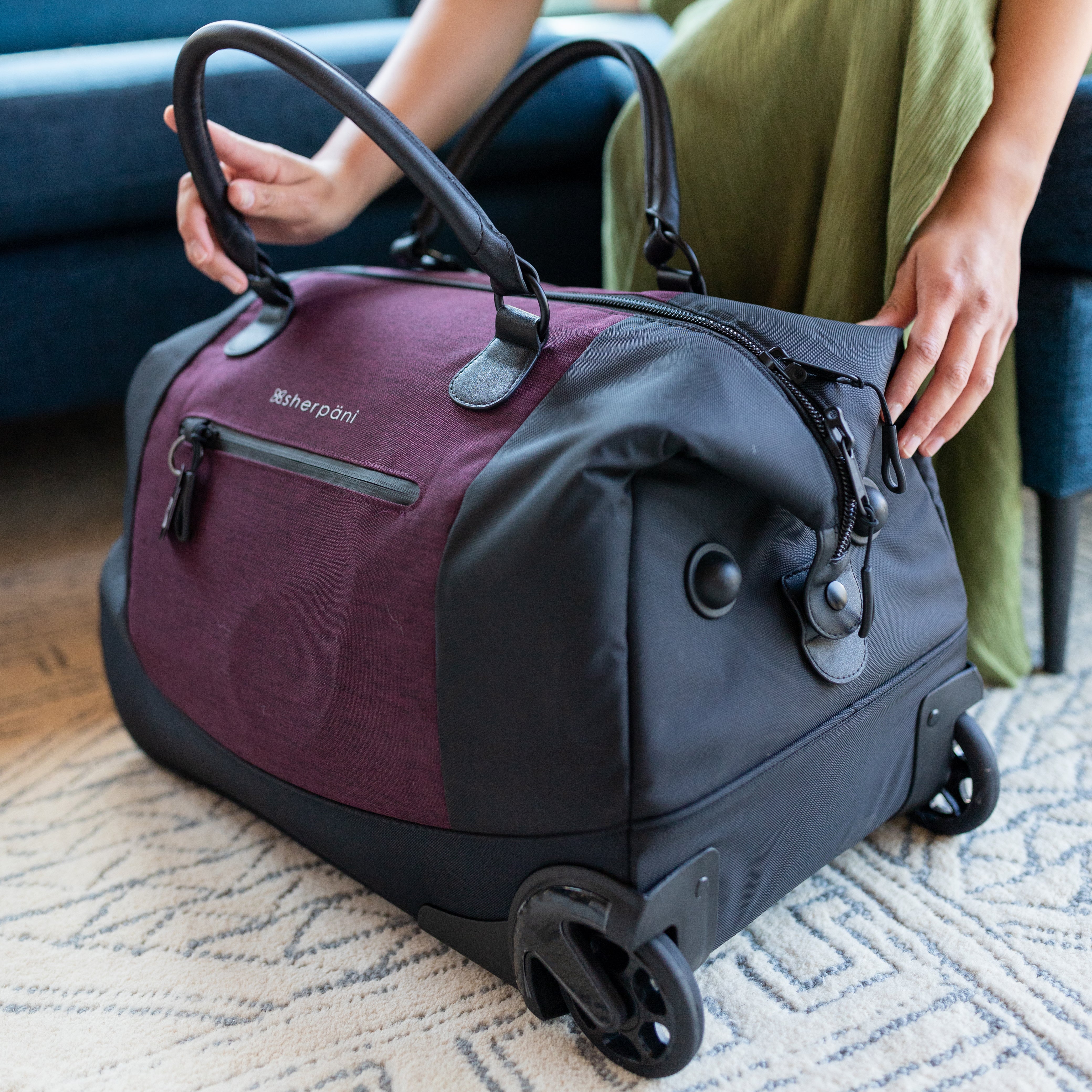 Close up view of Sherpani rolling duffle bag, the Trip in Merlot. Trip features include tote bag handles, retractable luggage handle, internal mesh pocket, internal zipper pocket, two external zipper pockets, Anti-Theft features and rolling wheels. 
