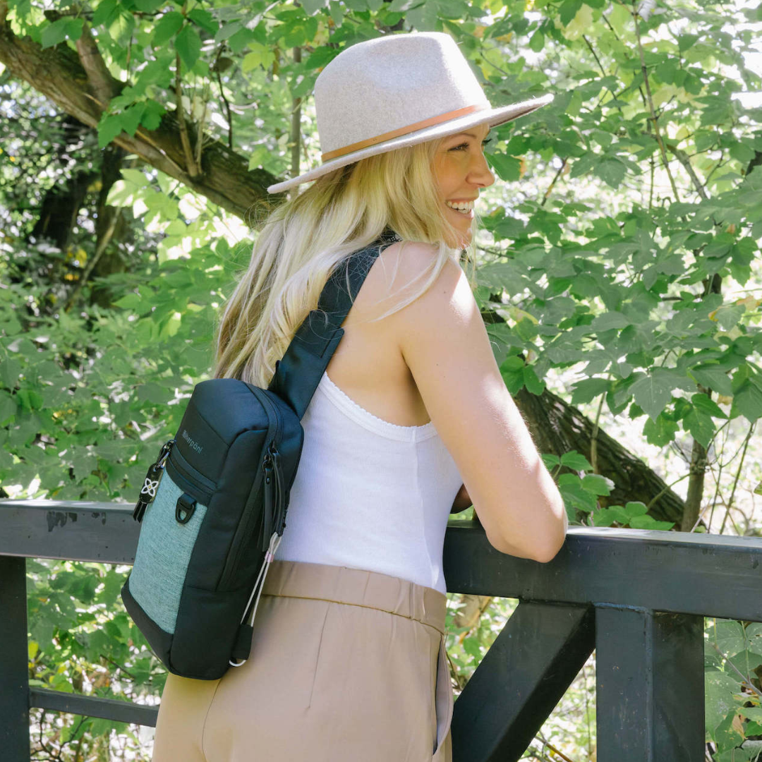 A woman leans on a railing outside wearing the Metro mini travel sling.