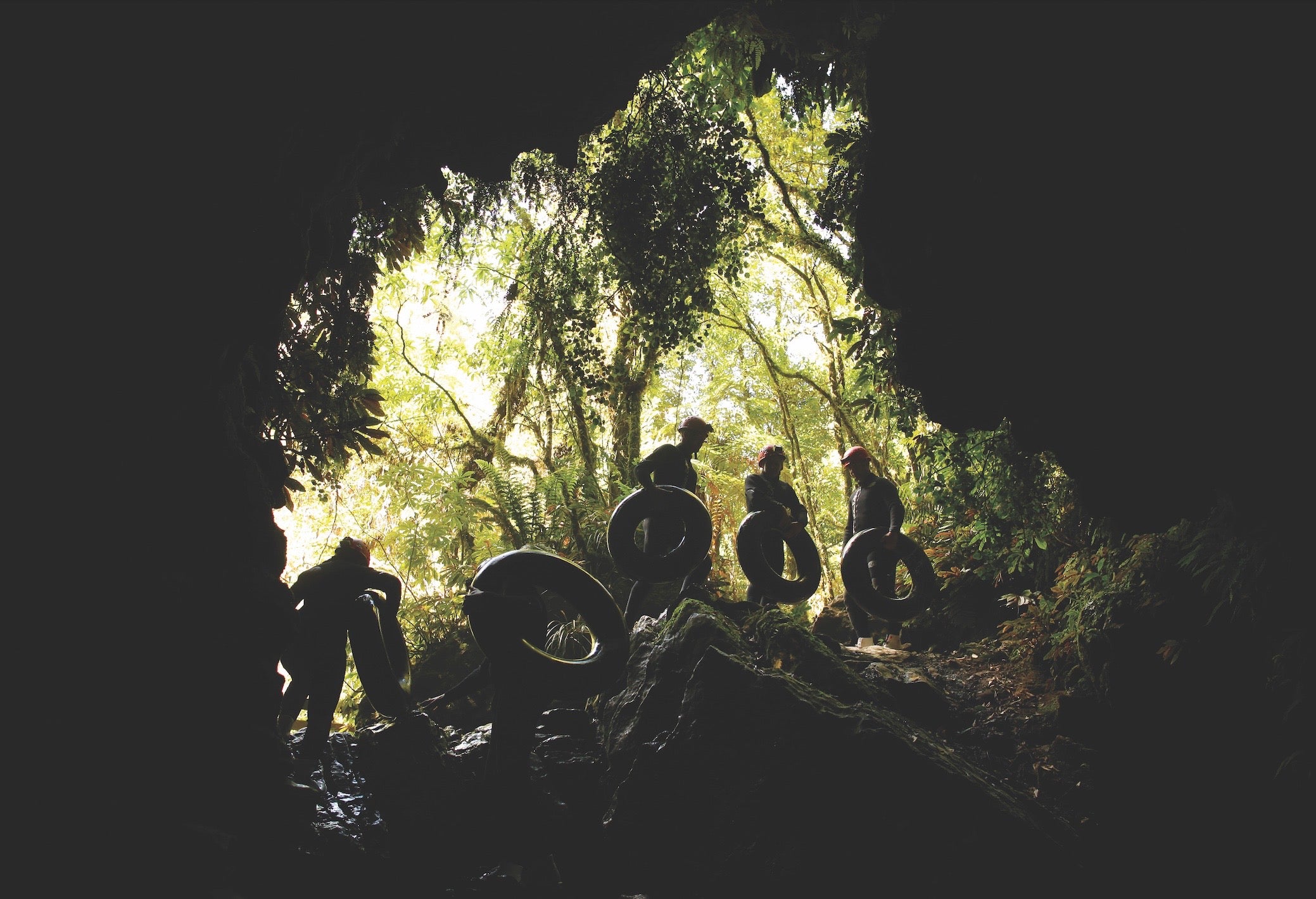 A group of explorers carry inner tubes and stand in the mouth of a cave
