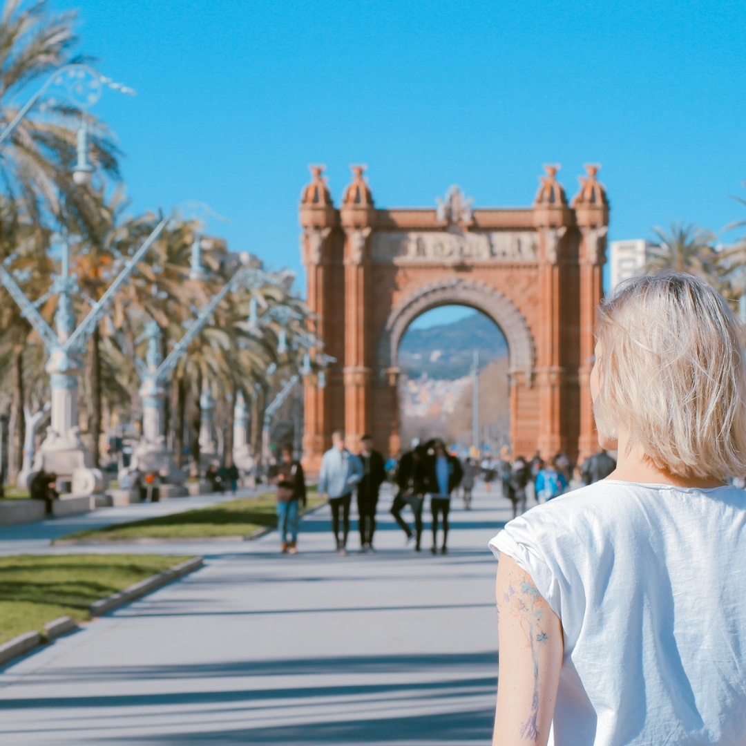 A blonde woman facing away from the camera is looking at a view of architecture and palm trees in Spain 