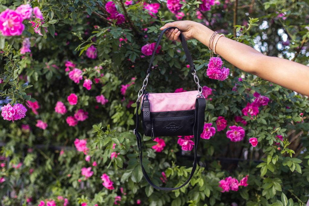 The Sherpani Skye small crossbody purse being held in front of a rose bush