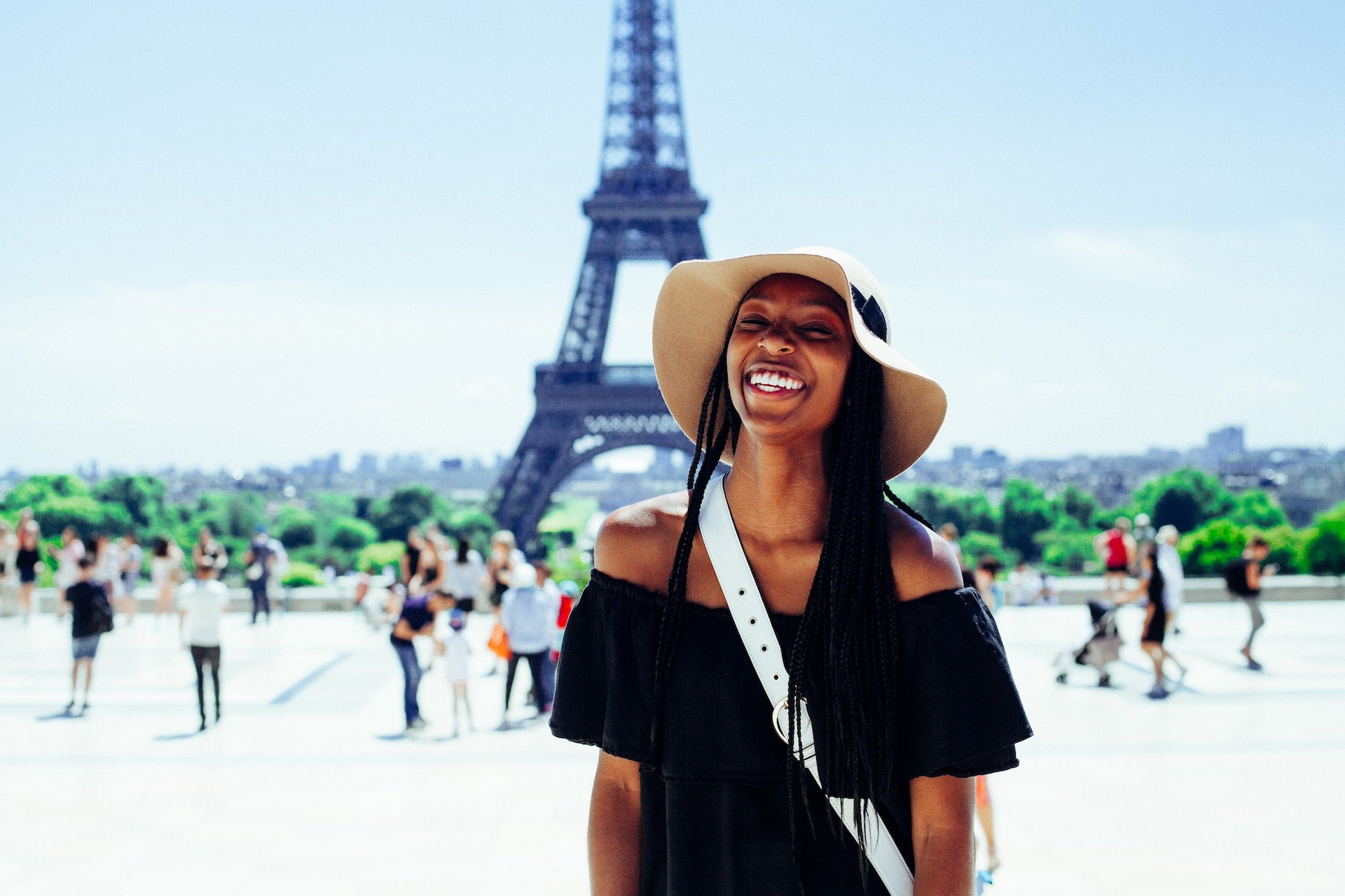 A black woman stands smiles at the camera with the Eiffel Tower behind her