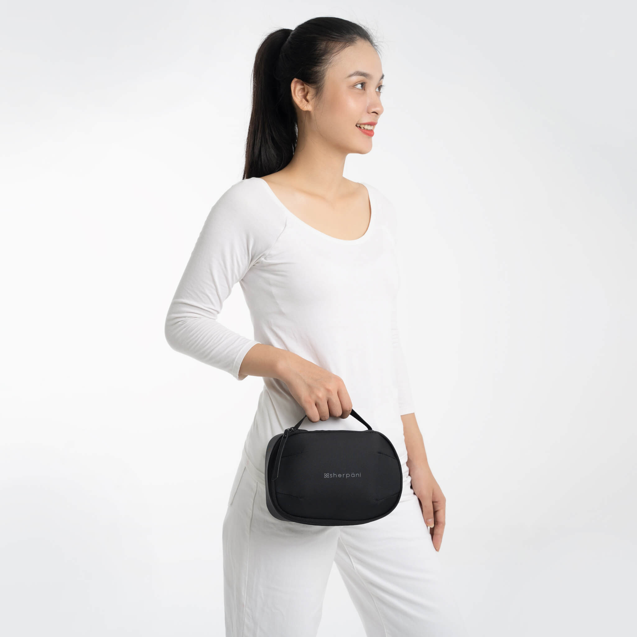 A model dressed in all white holds Sherpani travel accessory the Atlas in Carbon.