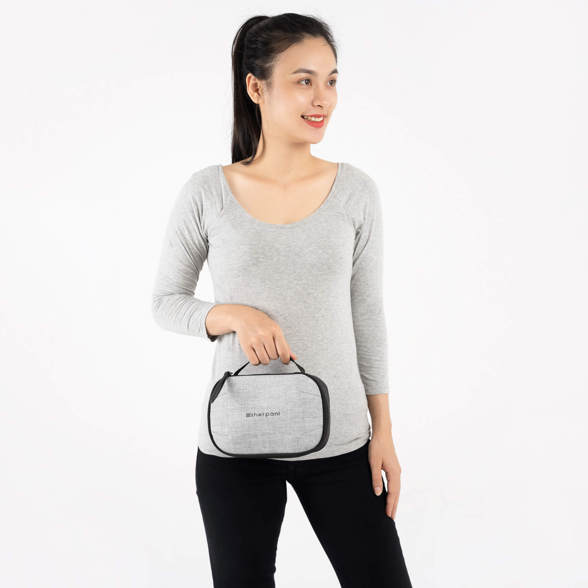 A model wearing black leggings and a gray top holds Sherpani travel accessory the Atlas in Sterling. 
