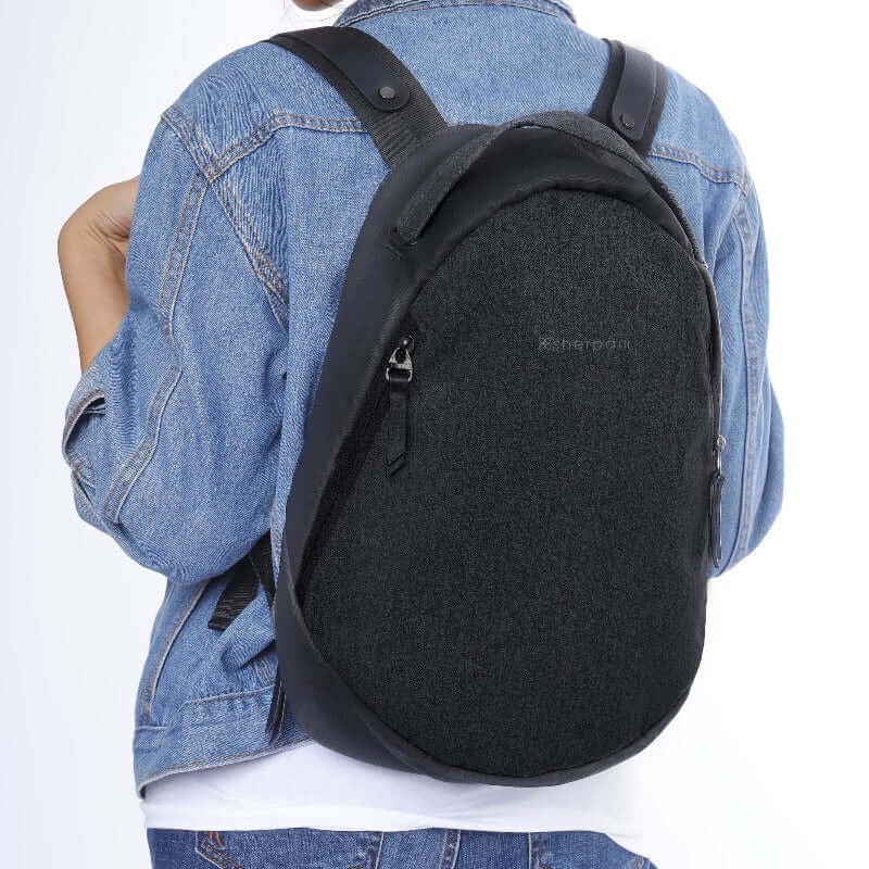 Close up view of a model wearing Sherpani's Anti-Theft backpack, the Presta in Black. She is wearing a jean jacket, a white shirt and jeans. 
