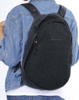 Close up view of a model wearing Sherpani's Anti-Theft backpack, the Presta in Black. She is wearing a jean jacket, a white shirt and jeans.