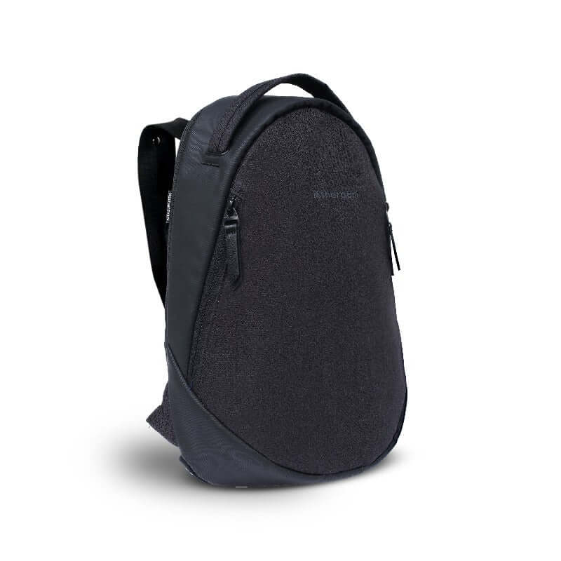 Angled front view of Sherpani's Anti-Theft backpack, the Presta in Black. There is an external zipper compartment on either side of the bag, an easy-access handle sits on the top and padded backpack straps are shown behind.