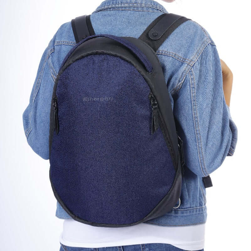 Close up view of a model wearing Sherpani&#39;s Anti-Theft backpack, the Presta in Midnight Blue. She is wearing a jean jacket, a white shirt and jeans.