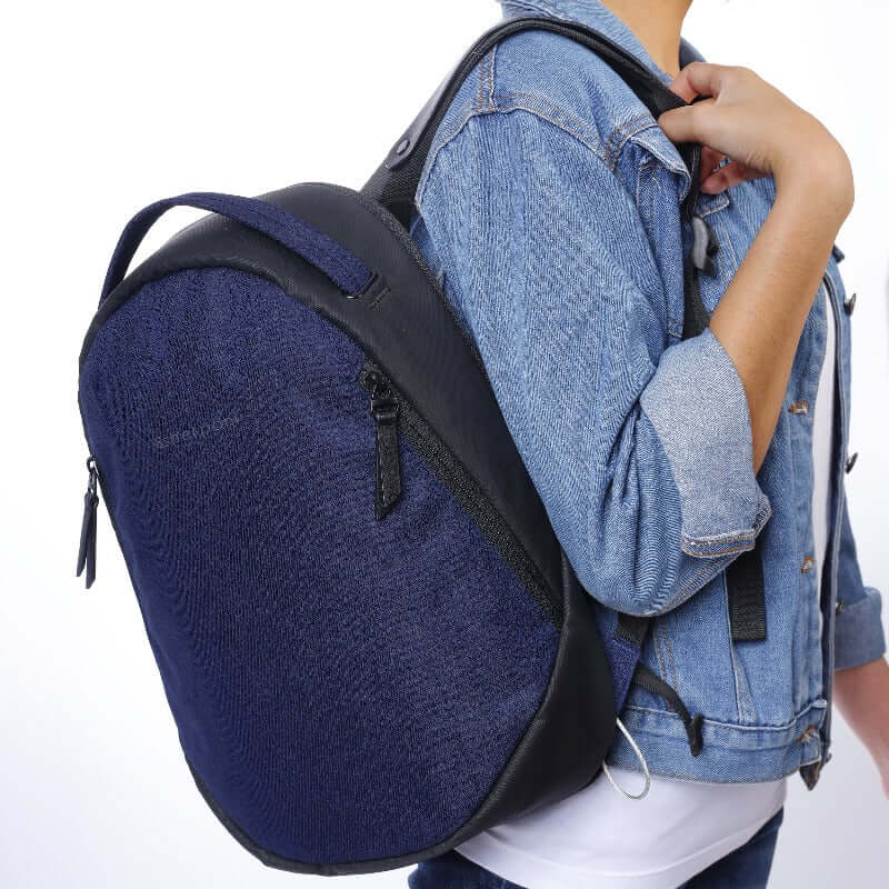 Close up view of a model wearing Sherpani's Anti-Theft backpack, the Presta in Midnight Blue, over one shoulder. She is wearing a jean jacket, a white shirt and jeans. 