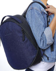Close up view of a model wearing Sherpani's Anti-Theft backpack, the Presta in Midnight Blue, over one shoulder. She is wearing a jean jacket, a white shirt and jeans.