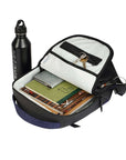 Sherpani's Anti-Theft backpack, the Presta in Midnight Blue, lies on its back. The main zipper compartment is open to reveal a light colored interior and internal zipper pocket. The bag is filled with example items: keys, wallet, notebook and magazines. A black Sherpani water bottle sits next to the bag.