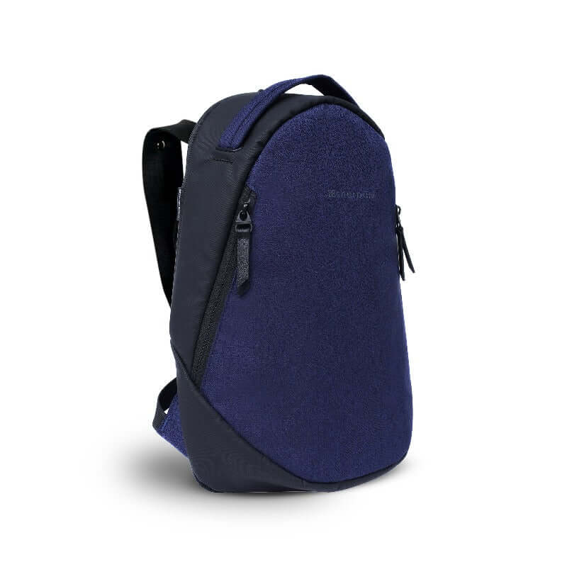 Angled front view of Sherpani&#39;s Anti-Theft backpack, the Presta in Midnight Blue, with black accents. There is an external zipper compartment on either side of the bag, an easy-access handle sits on the top and padded backpack straps are shown behind.