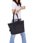 A brown haired model faces the side. She is wearing a white tee shirt and jeans. Her elbow is hooked through the handles of Sherpani's Anti-Theft tote the Cali AT in Carbon.