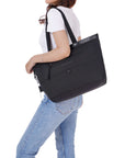 A brown haired model is facing the side. She is wearing a white tee shirt and jeans. Sherpani's Anti-Theft tote the Cali AT in Carbon sits on her shoulder.