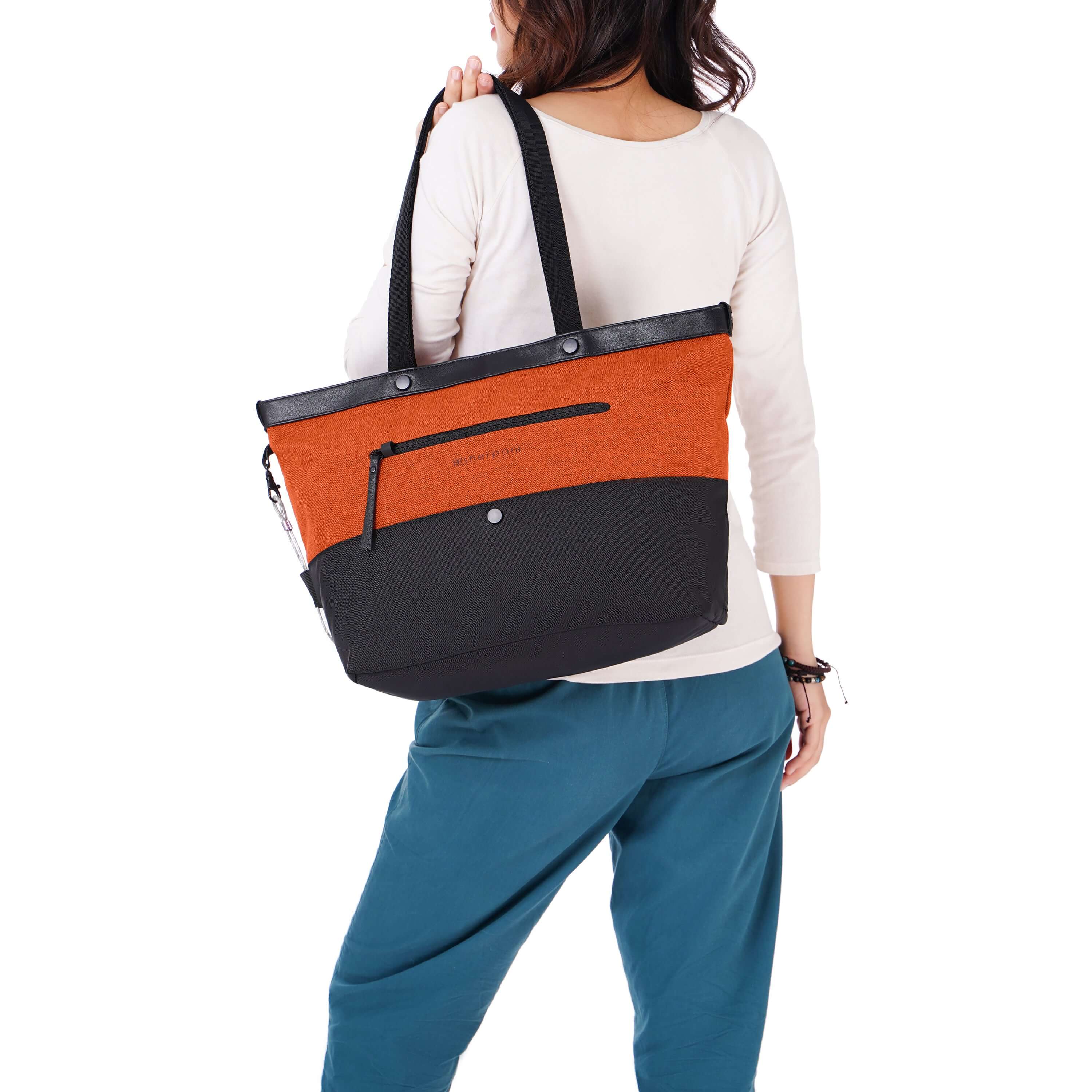 Close up view of dark haired model facing away from the camera. She is wearing a white shirt and blue pants. She is carrying Sherpani&#39;s Anti-Theft tote the Cali AT in Copper over her shoulder.