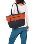 Close up view of dark haired model facing away from the camera. She is wearing a white shirt and blue pants. She is carrying Sherpani's Anti-Theft tote the Cali AT in Copper over her shoulder.