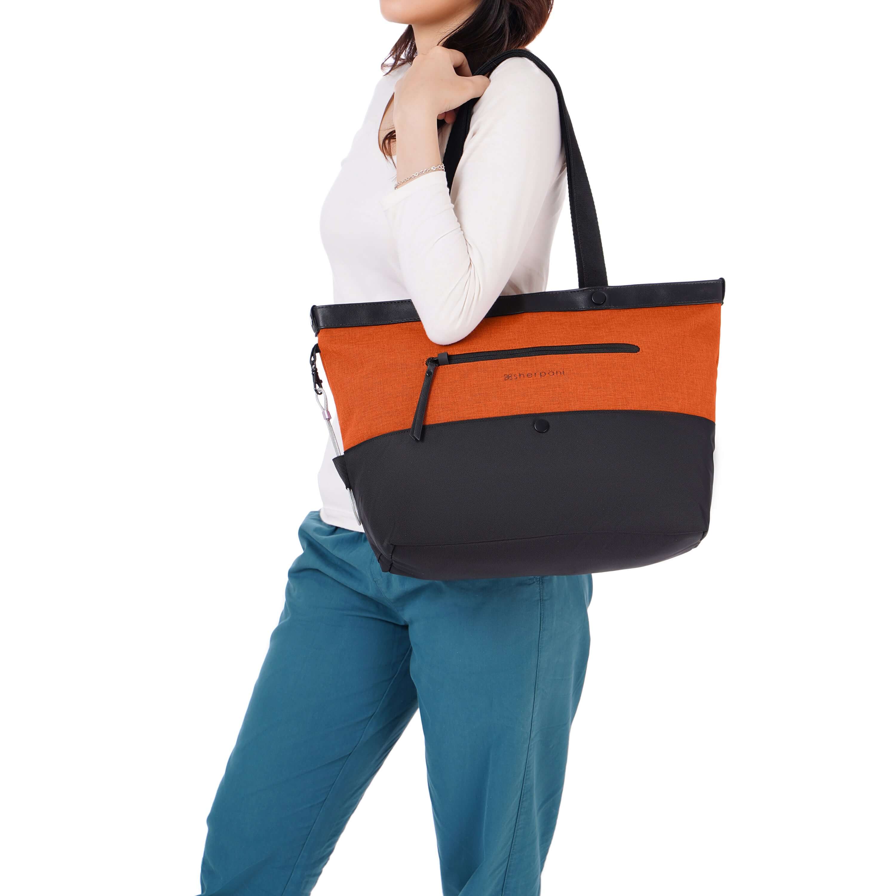 Close up view of dark haired model facing the side. She is wearing a white shirt and blue pants. Over her shoulder sits Sherpani&#39;s Anti-Theft tote the Cali AT in Copper.