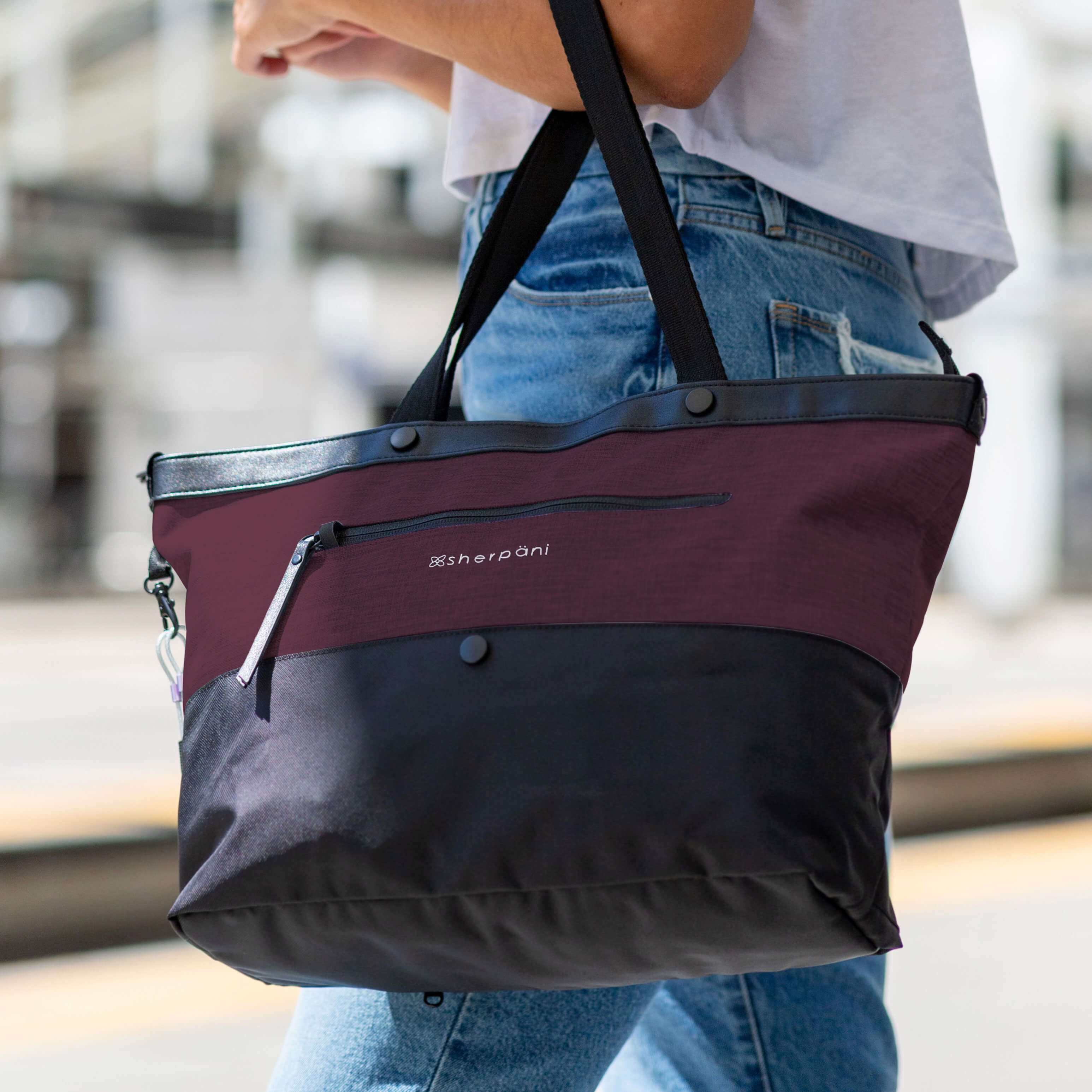 Close up view of a woman carrying Sherpani Anti-Theft tote bag, the Cali in Merlot, by her side. 