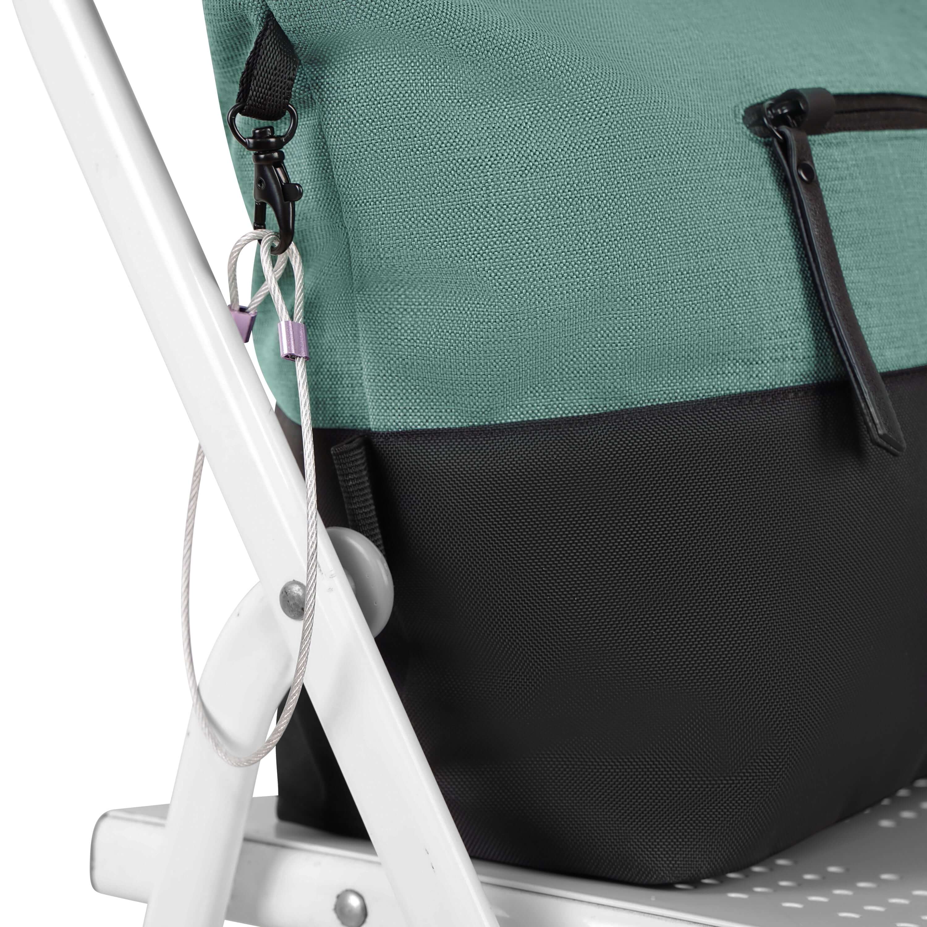 Close up side view of Sherpani's Anti-Theft tote the Cali AT in Teal. The bag is sitting on a white chair and is secured to the chair by the wire-loop chair lock.