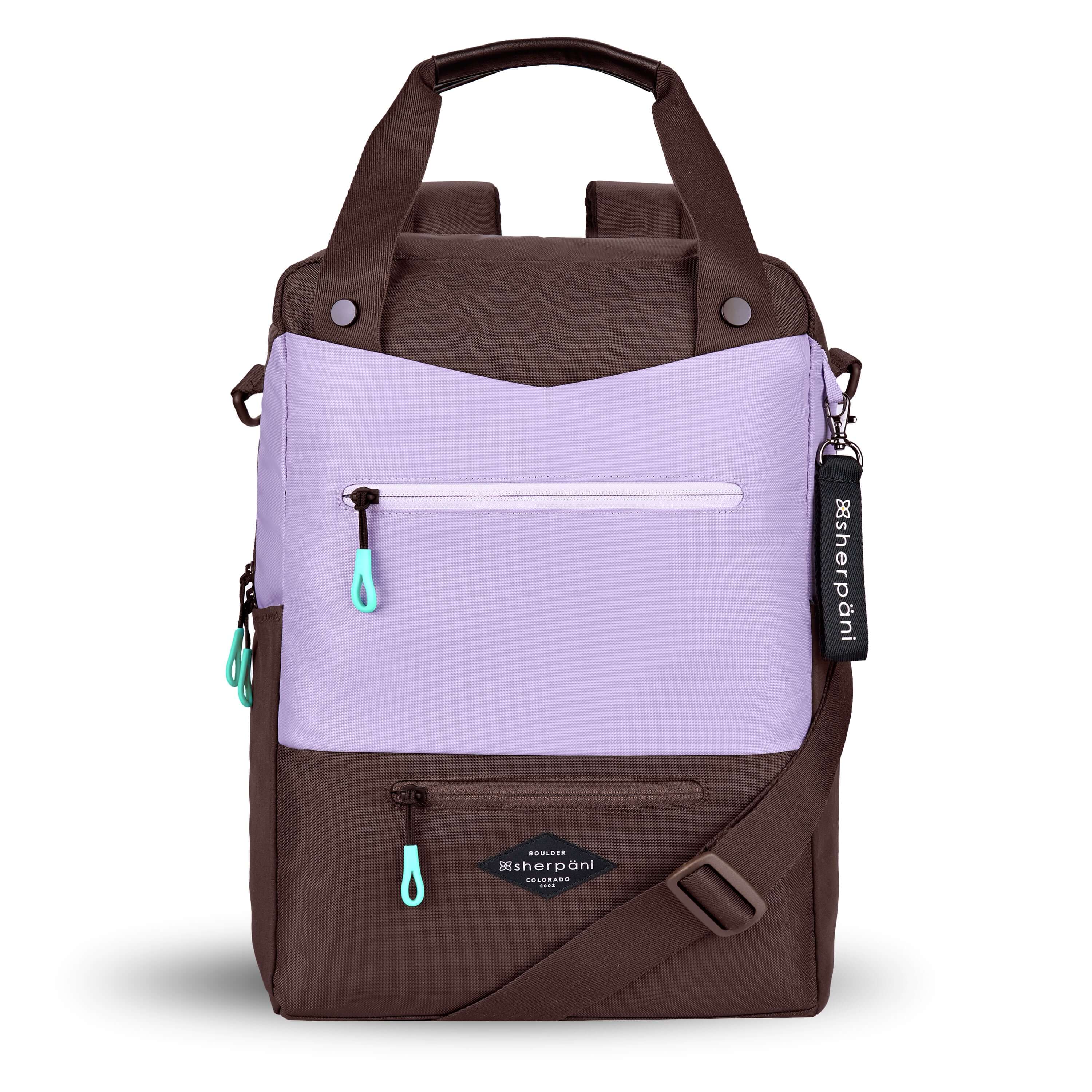 Flat front view of Sherpani&#39;s three-in-one bag, the Camden in Lavender. The bag is two-toned in lavender and brown. There are two external zipper pockets on the front panel with easy-pull zippers in aqua. A branded Sherpani keychain is clipped to the upper right corner. An elastic water bottle holder sits on either side of the bag. The bag has an adjustable/detachable crossbody strap, padded/adjustable backpack straps and short tote handles fixed at the top.