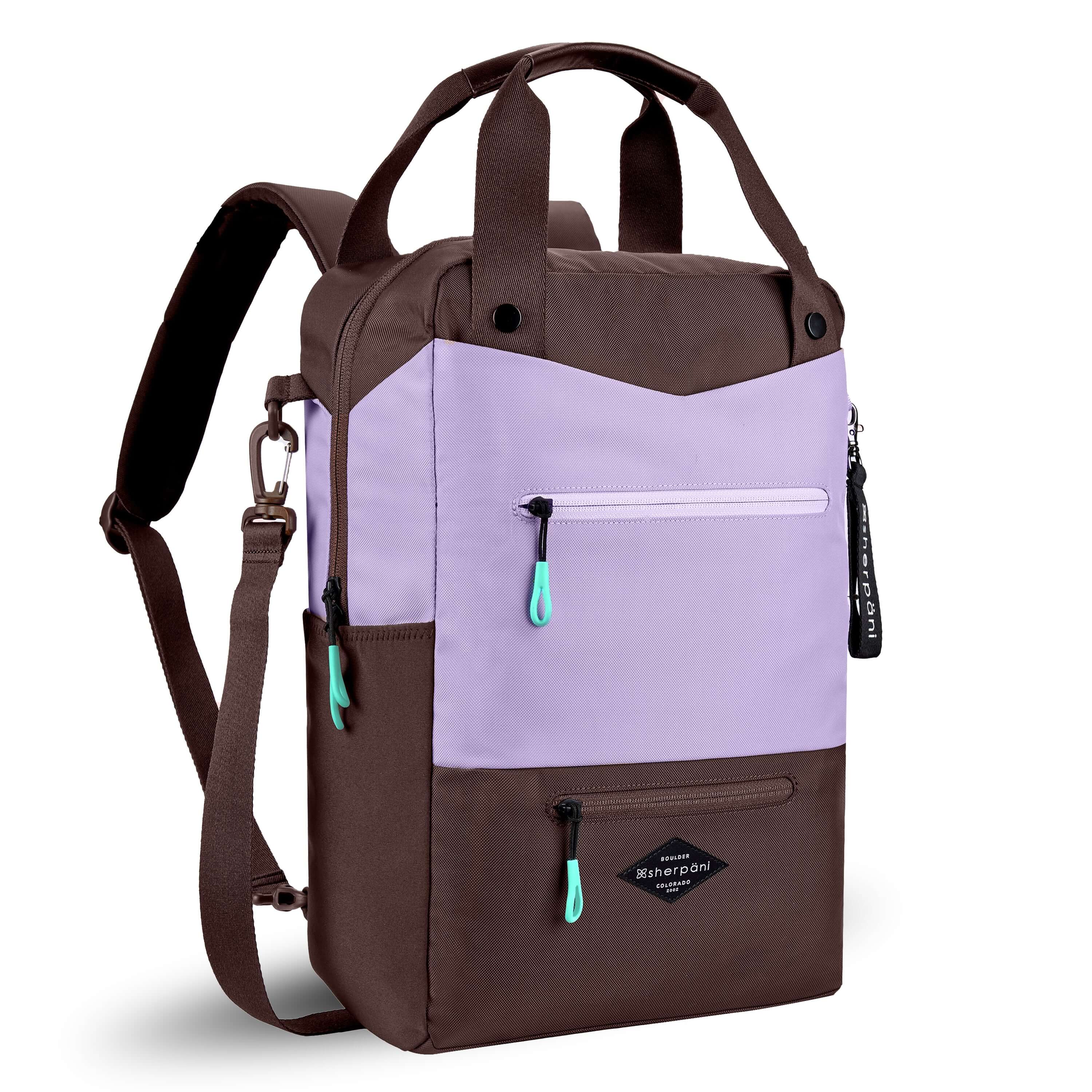 Angled front view of Sherpani's three-in-one bag, the Camden in Lavender. The bag is two-toned in lavender and brown. There are two external zipper pockets on the front panel with easy-pull zippers in aqua. A branded Sherpani keychain is clipped to the upper right corner. An elastic water bottle holder sits on either side of the bag. The bag has an adjustable/detachable crossbody strap, padded/adjustable backpack straps and short tote handles fixed at the top. 