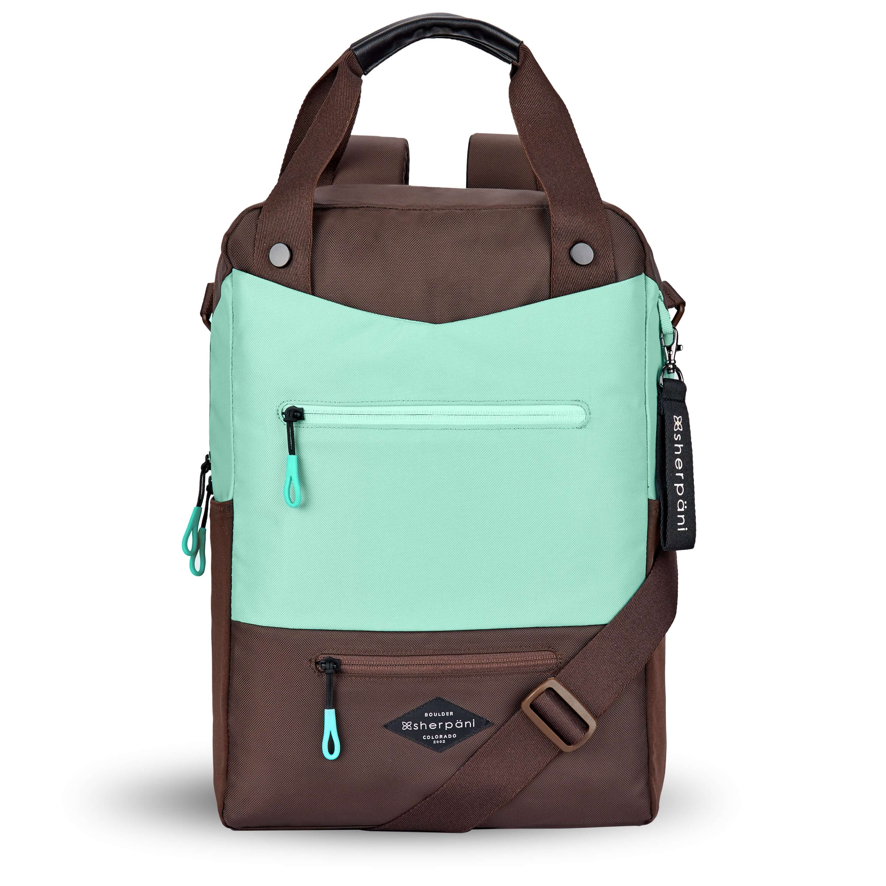 Flat front view of Sherpani's three-in-one bag, the Camden in Seagreen. The bag is two-toned in light green and brown. There are two external zipper pockets on the front panel with easy-pull zippers in light green. A branded Sherpani keychain is clipped to the upper right corner. An elastic water bottle holder sits on either side of the bag. The bag has an adjustable/detachable crossbody strap, padded/adjustable backpack straps and short tote handles fixed at the top. 