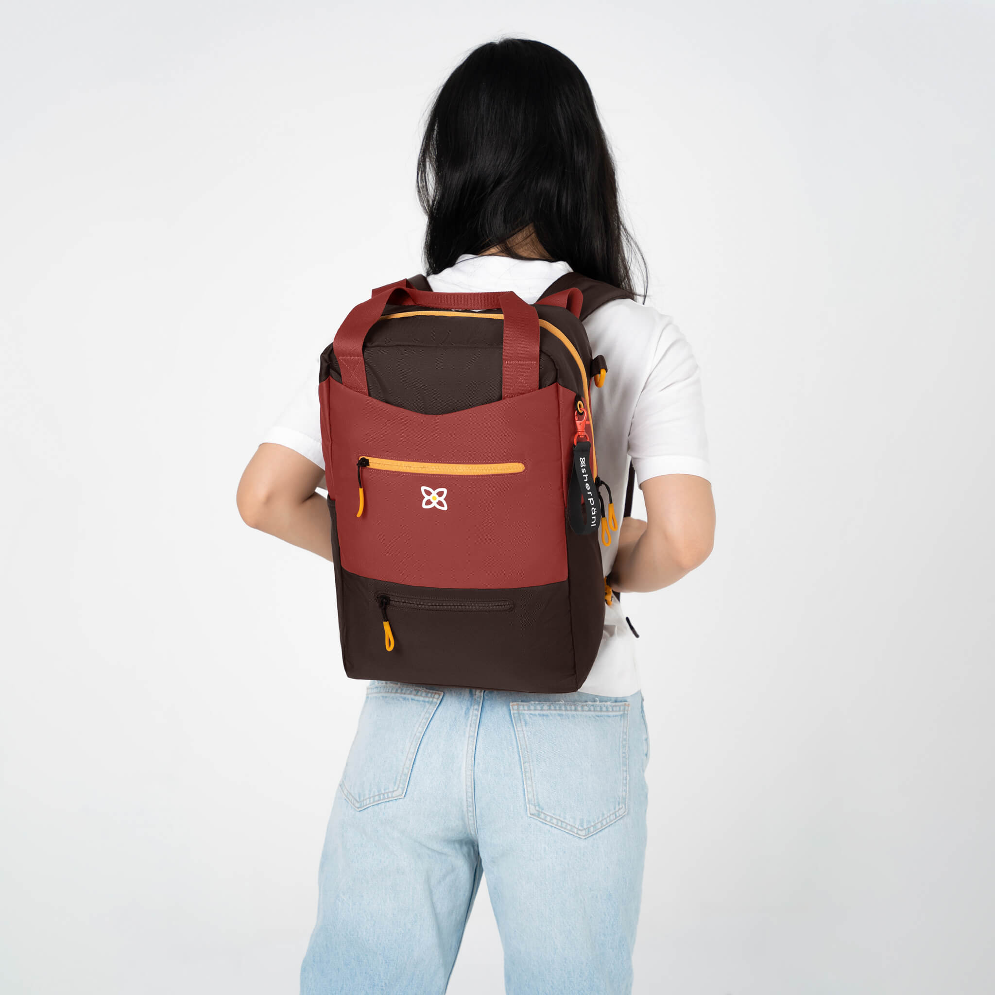 A model wearing Sherpani personal item backpack, the Camden in Cider. 