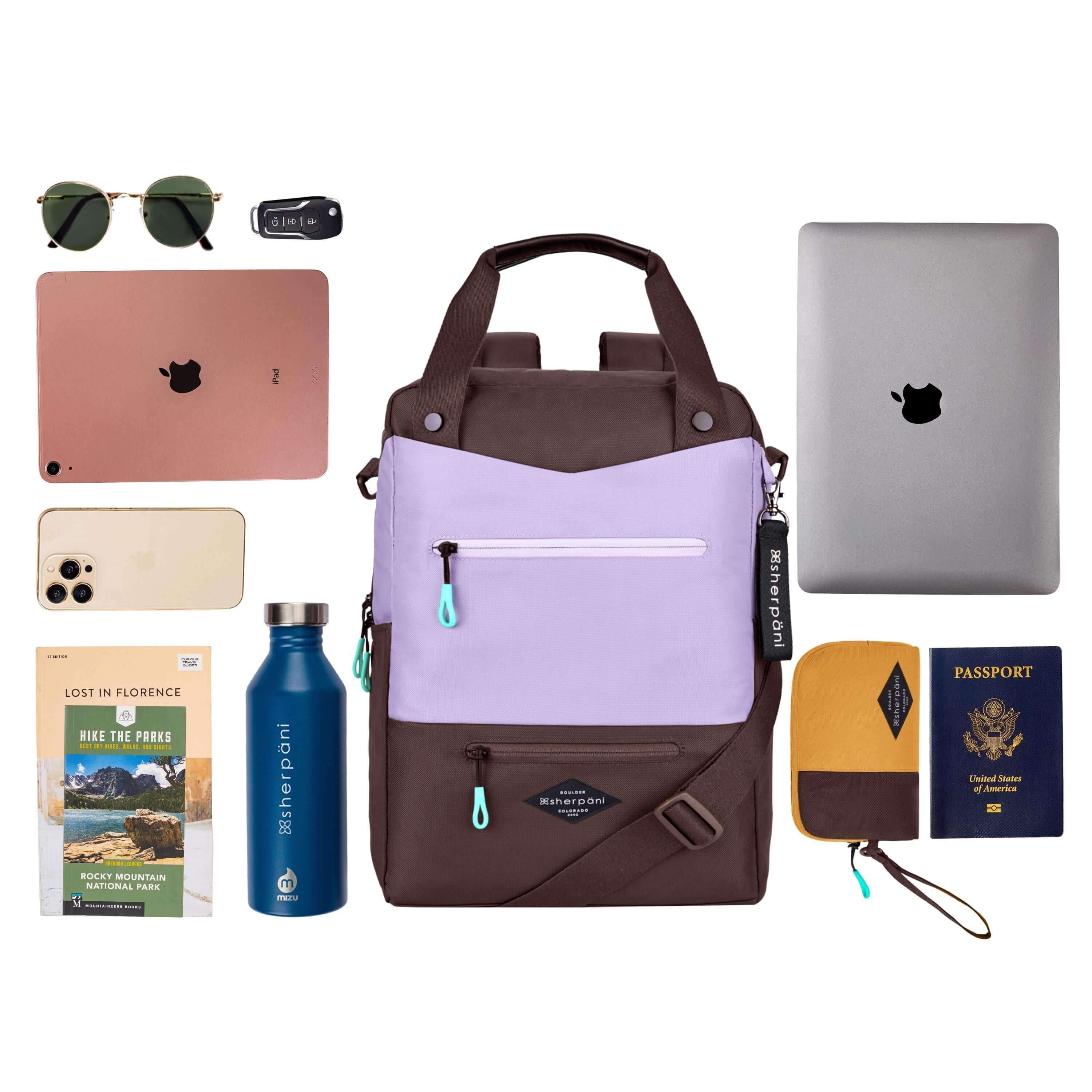 Top view of example items to fill the bag. Sherpani&#39;s three-in-one bag, the Camden in Lavender, lies in the center. It is surrounded by an assortment of items: sunglasses, car key, tablet, phone, travel books, water bottle, laptop, passport and Sherpani travel accessory the Jolie in Sundial.