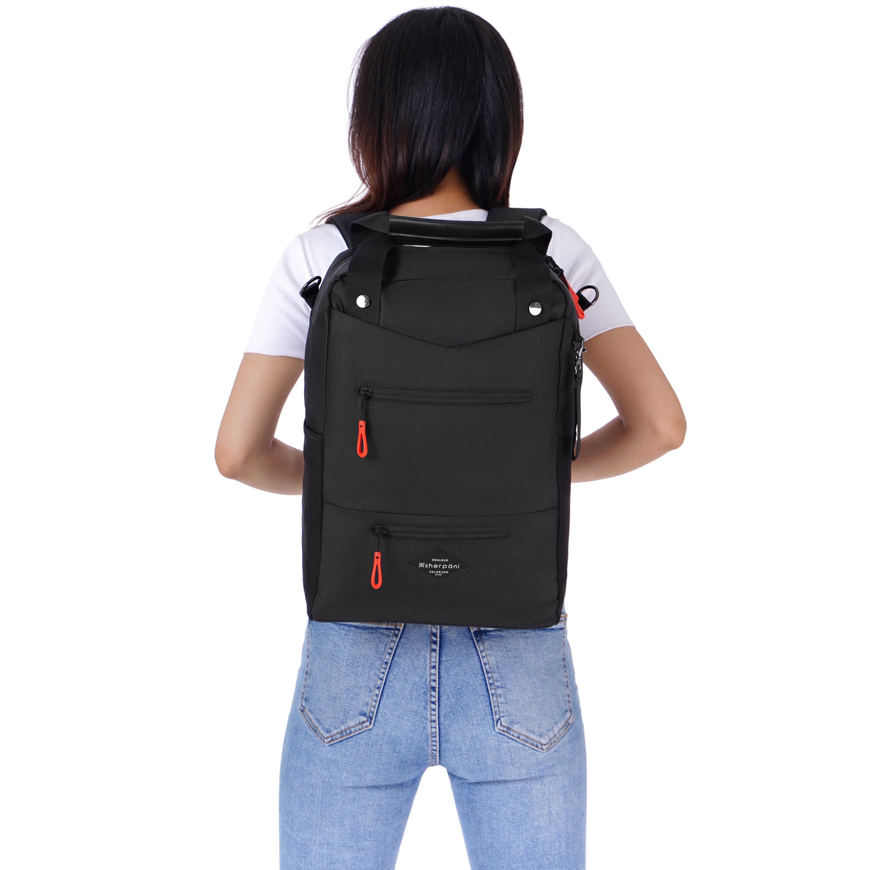 Close up view of a dark haired model facing away from the camera. She is wearing a white tee shirt and jeans. She is carrying Sherpani&#39;s three-in-one bag, the Camden in Raven, as a backpack.