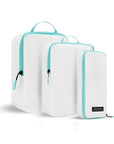 Angled front view of the Compass Packing Cubes in three sizes: small, medium and large. The cubes are white with zipper and handle accented in aqua.