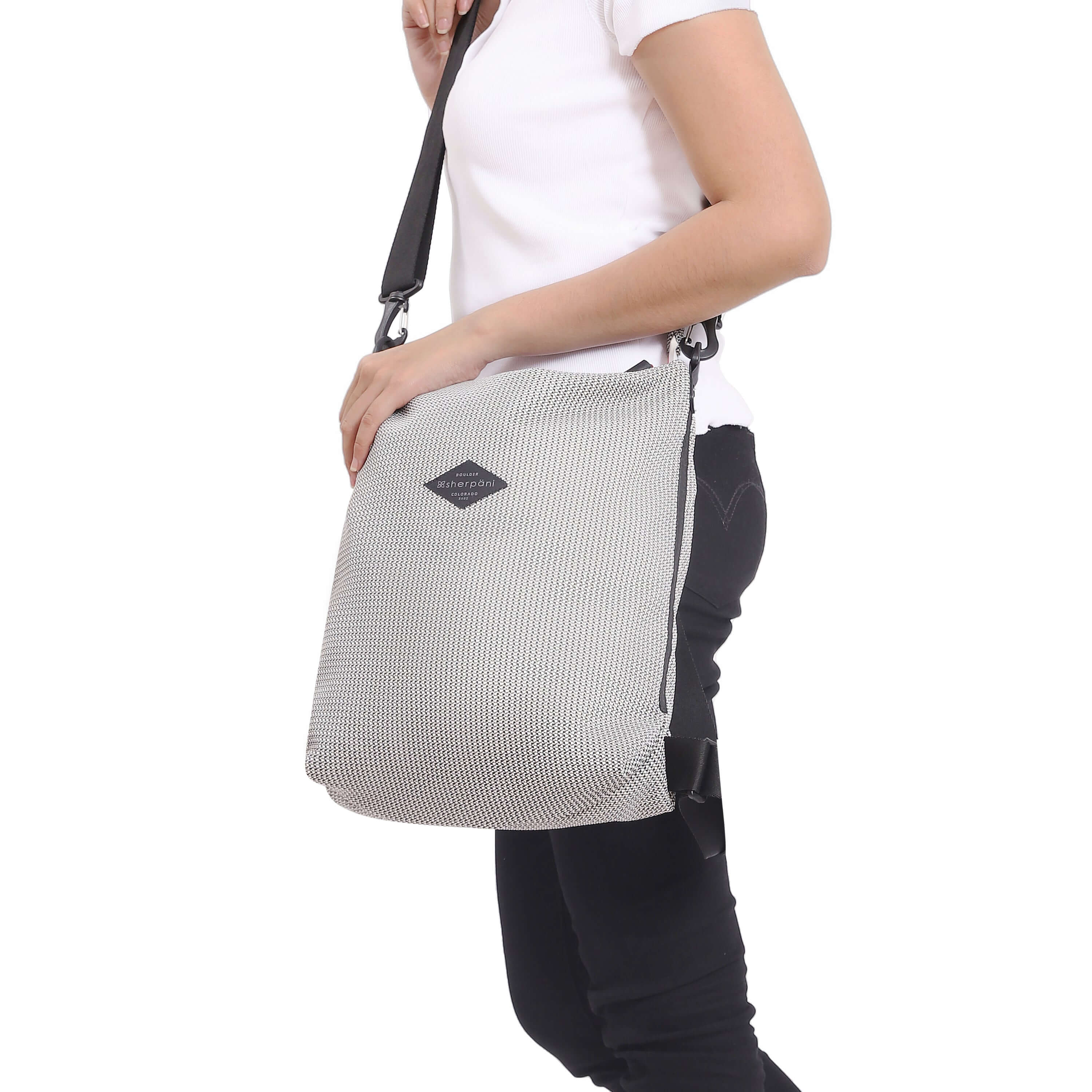Close up view of a model facing the side. She is wearing a white tee shirt and black pants. She carries Sherpani mesh convertible bag, the Delanie, as a crossbody.